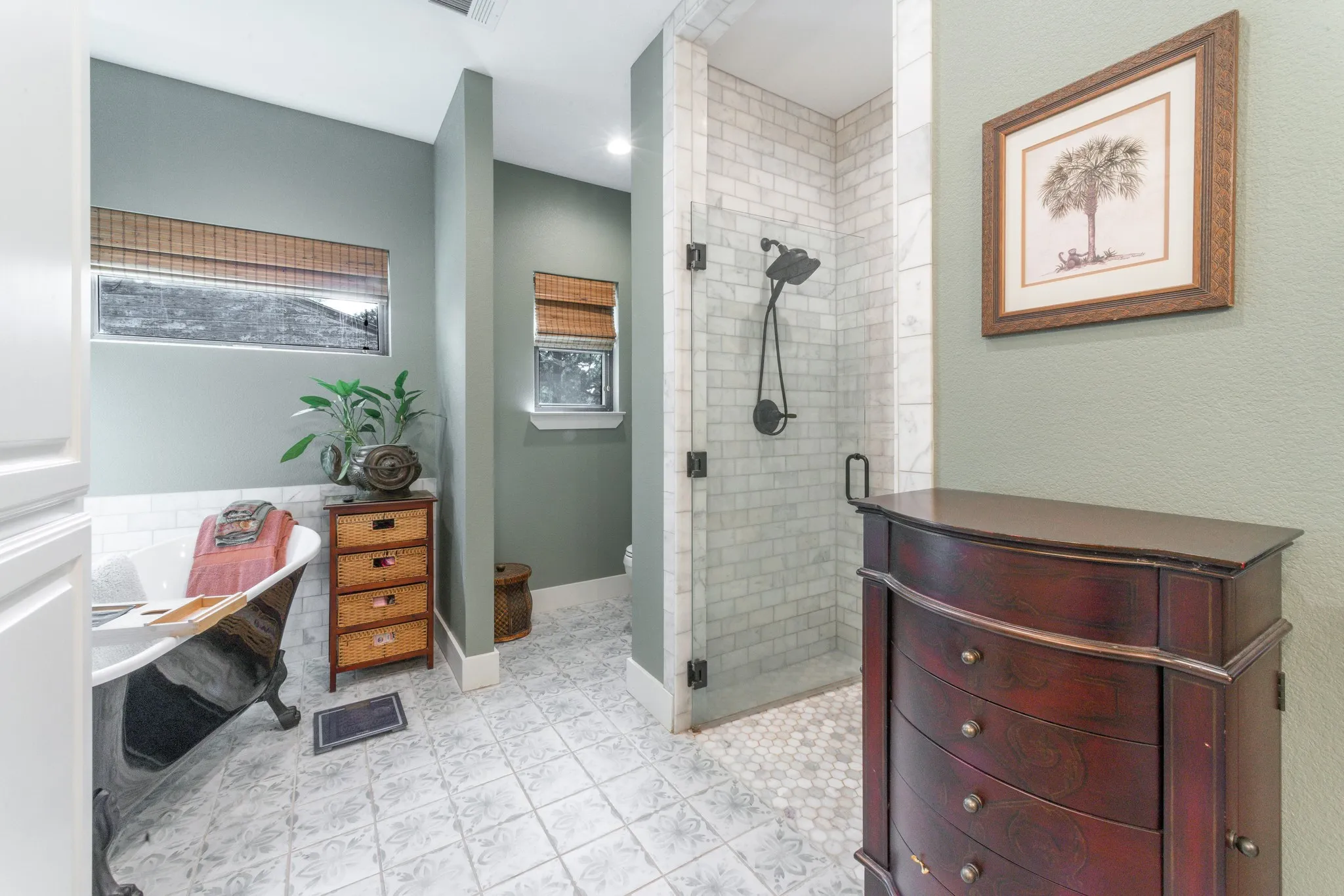 Bathroom featuring a freestanding clawfoot tub, a walk-in shower with subway tile surround, patterned floor tile, and a framed window with a woven wood blind