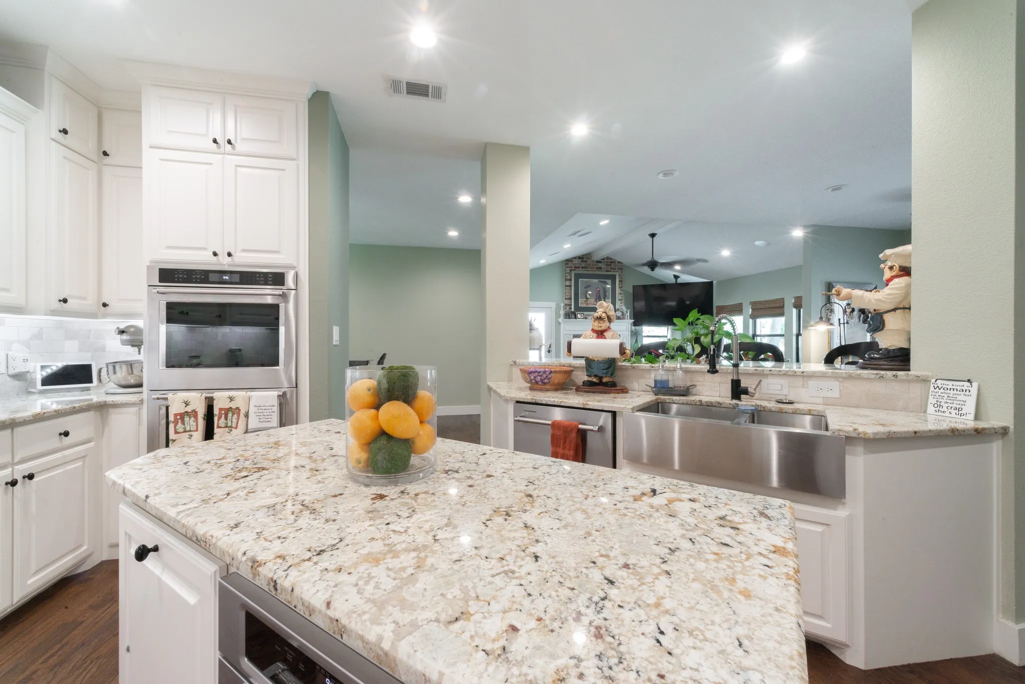 Gourmet kitchen featuring a large island with a light-toned granite countertop, stainless steel double oven, white shaker-style cabinetry, and wood-finish flooring