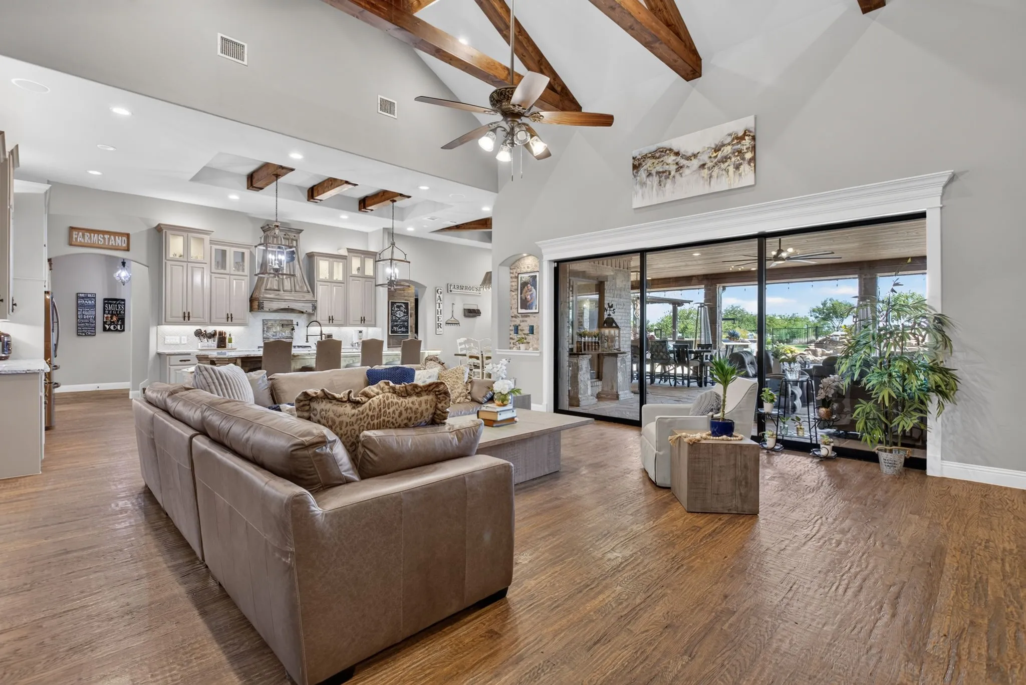 Expansive living area with wood-finish flooring, vaulted ceilings featuring exposed wood beams, and a ceiling fan
