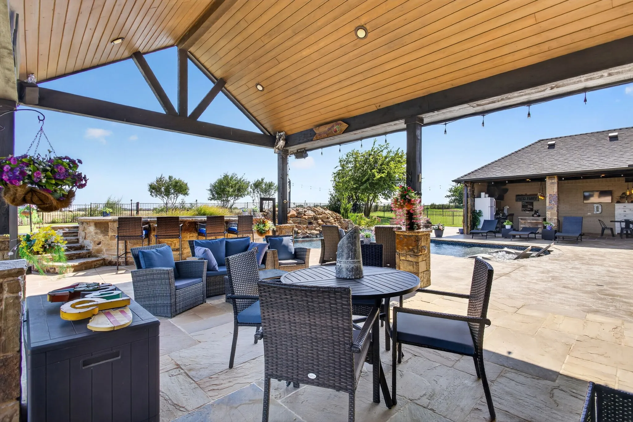 Expansive covered patio featuring a wood-finish vaulted ceiling, recessed lighting, and a built-in stone bar with seating