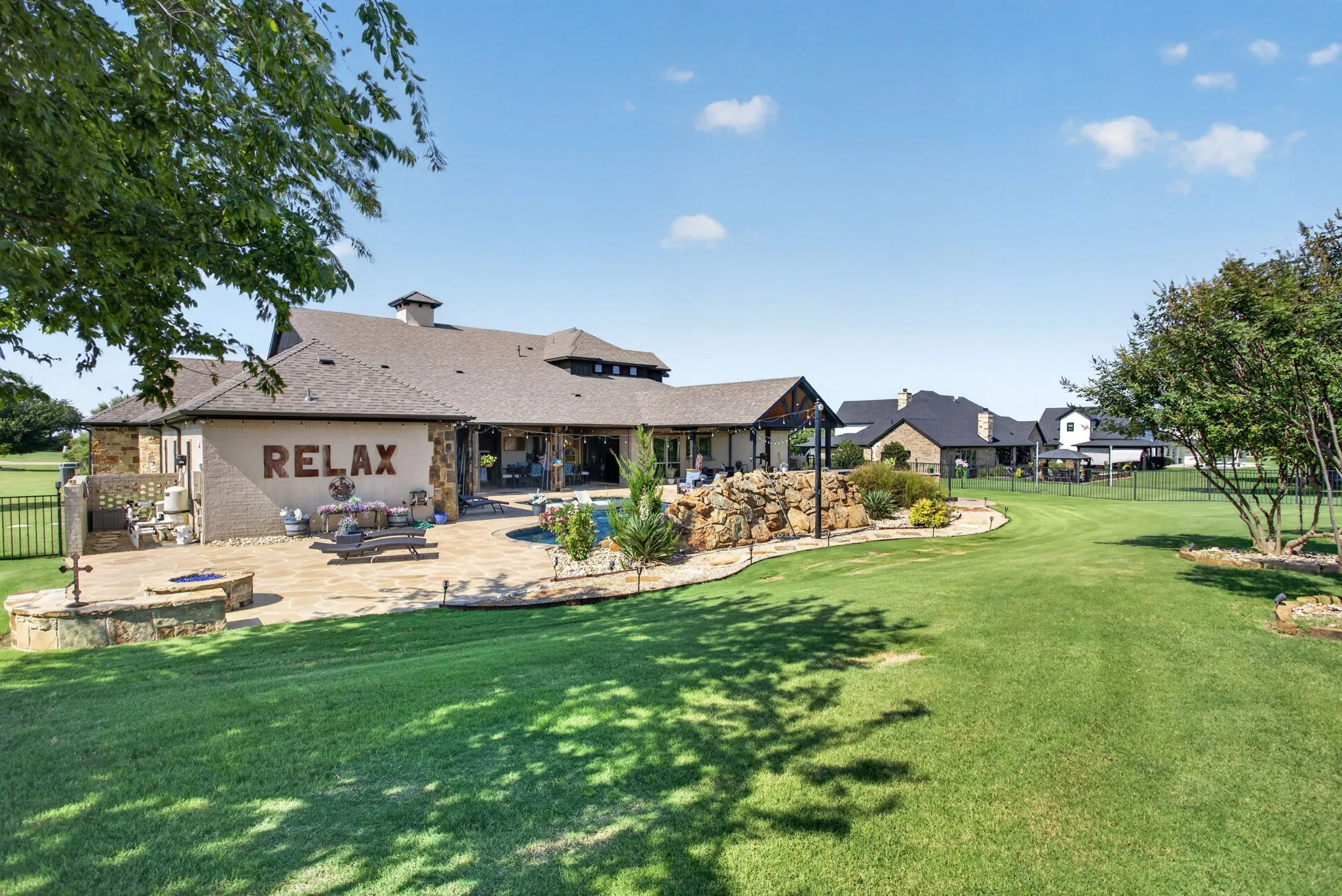 Expansive lawn with a stone-clad patio, built-in fire pit, and a swimming pool