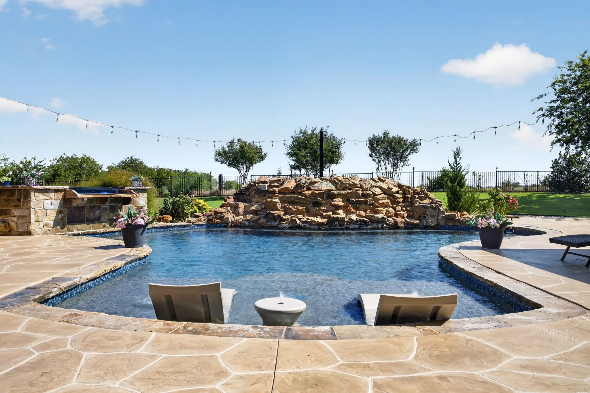 Resort-style pool area featuring a natural rock waterfall, integrated spa with stone surround, and an expansive flagstone patio