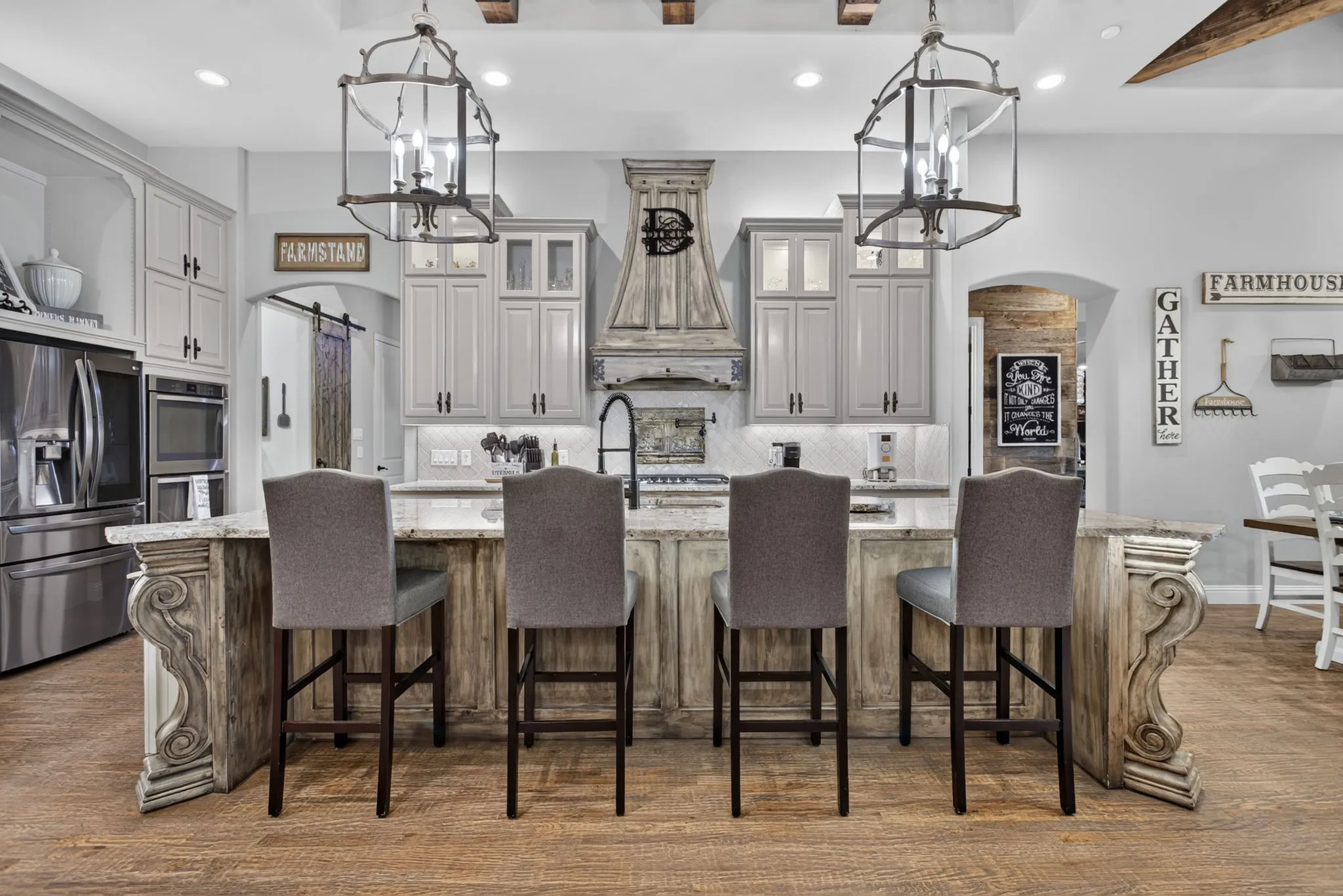 Kitchen island featuring a light-toned countertop, distressed wood-finish base with ornate carved accents, and four upholstered bar stools