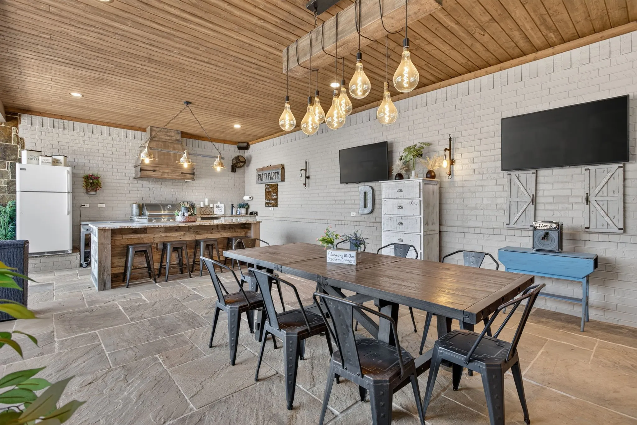 Covered outdoor living space featuring stone flooring, a wood-paneled ceiling, and white brick walls