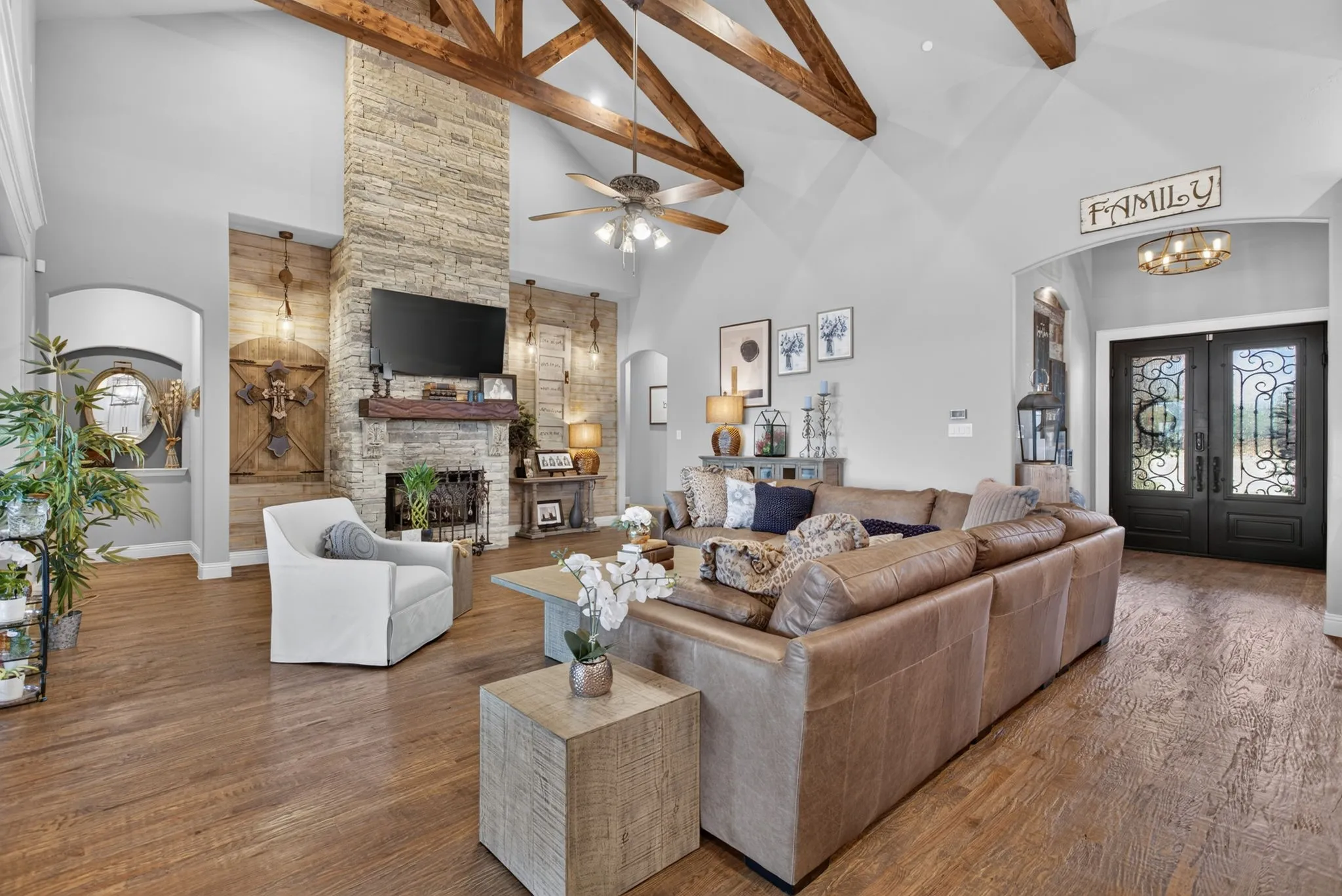 Vaulted ceiling with exposed wood beams, stone fireplace extending to the ceiling, wood-finish flooring, double front entry doors with decorative ironwork, and an arched entry