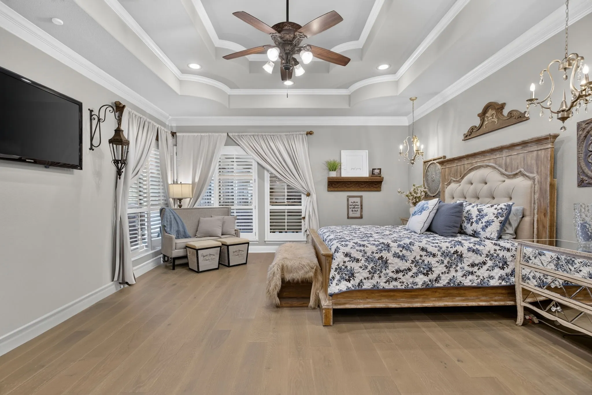 Spacious room featuring wood-finish flooring, a tray ceiling with recessed lighting and a ceiling fan, and multiple windows with plantation shutters