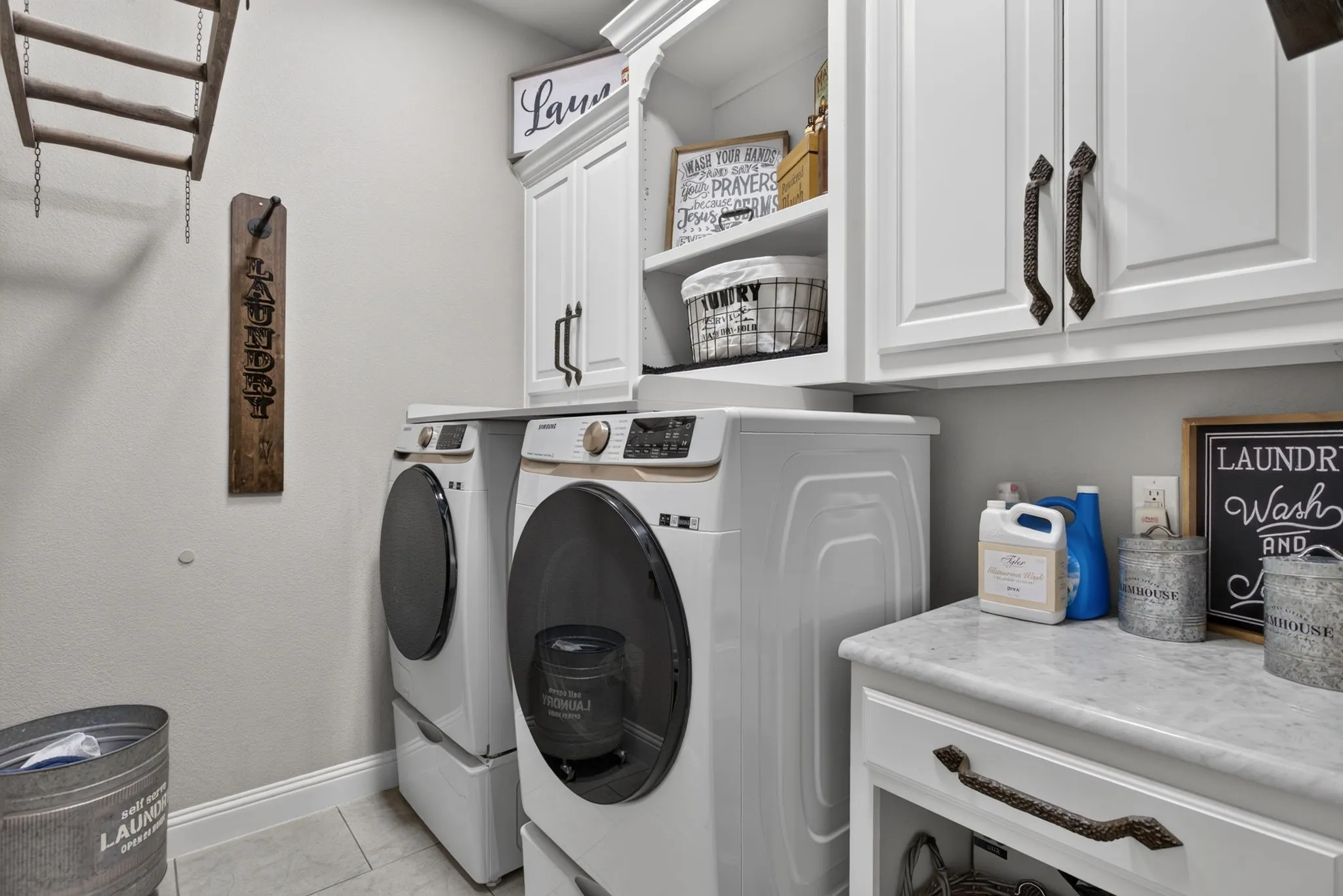 Dedicated laundry space featuring side-by-side appliances, white cabinetry with dark hardware, and a light-toned countertop