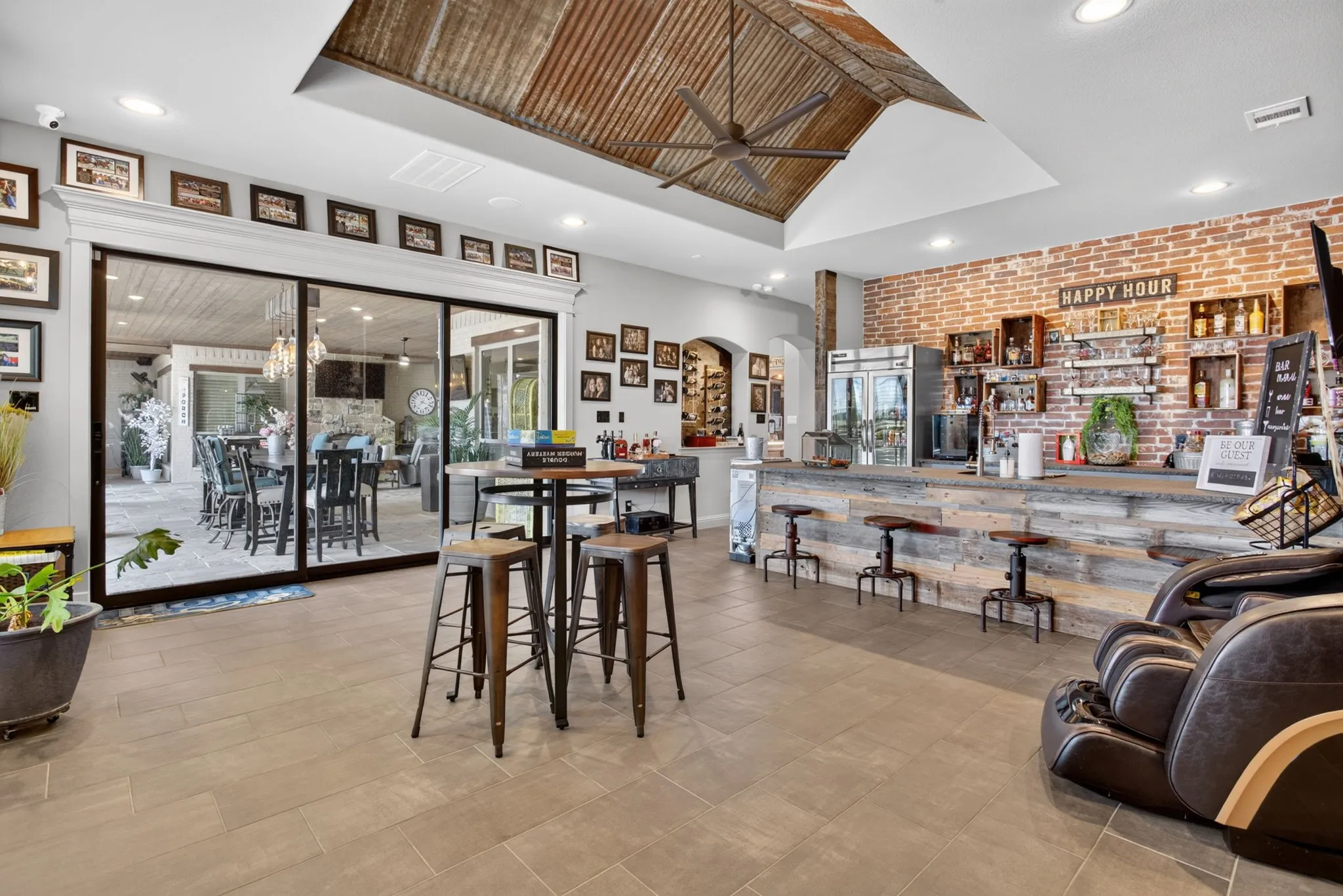 Spacious entertainment area featuring a reclaimed wood bar, exposed brick accent wall, and a corrugated metal vaulted ceiling