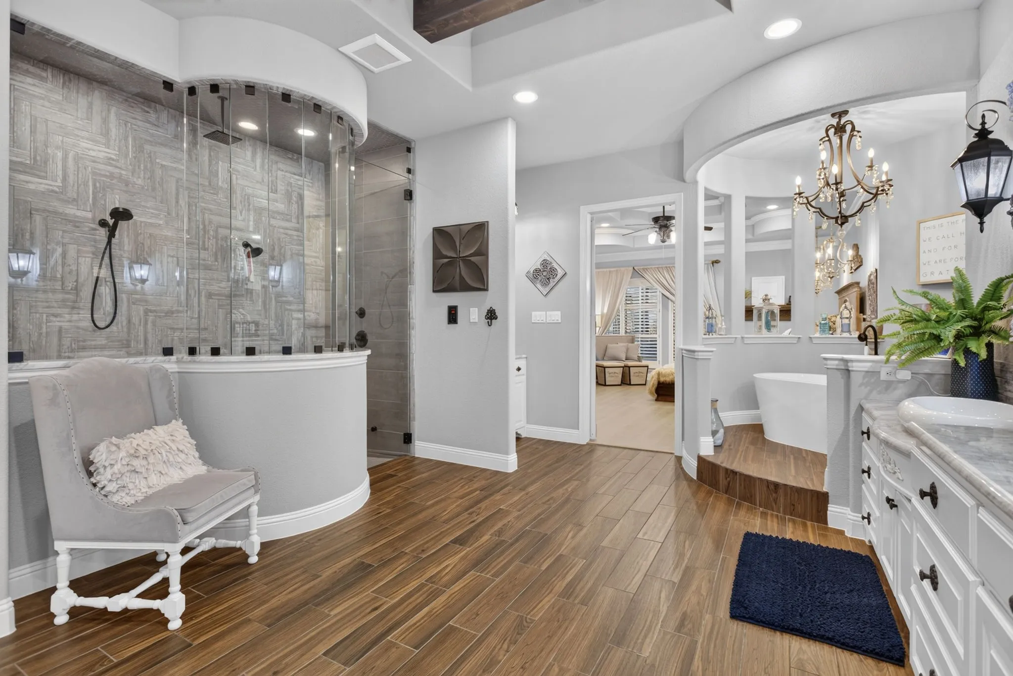 Spacious bathroom featuring wood-finish flooring, a curved glass shower enclosure with textured tile walls, and recessed lighting