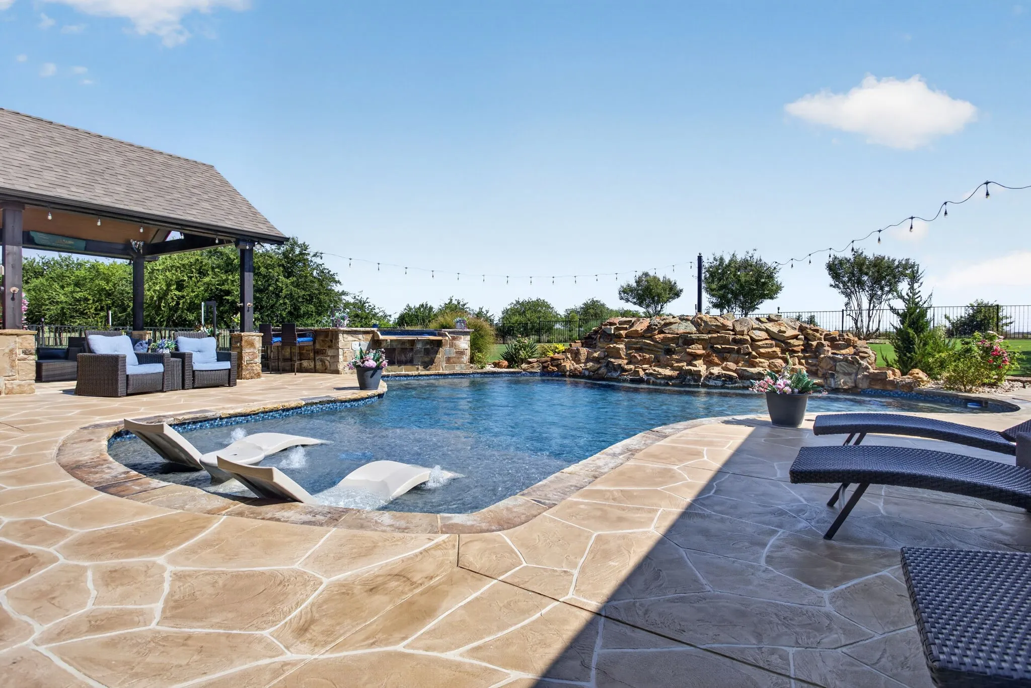 Custom-shaped swimming pool featuring an integrated water feature with natural stone and an expansive stamped concrete patio