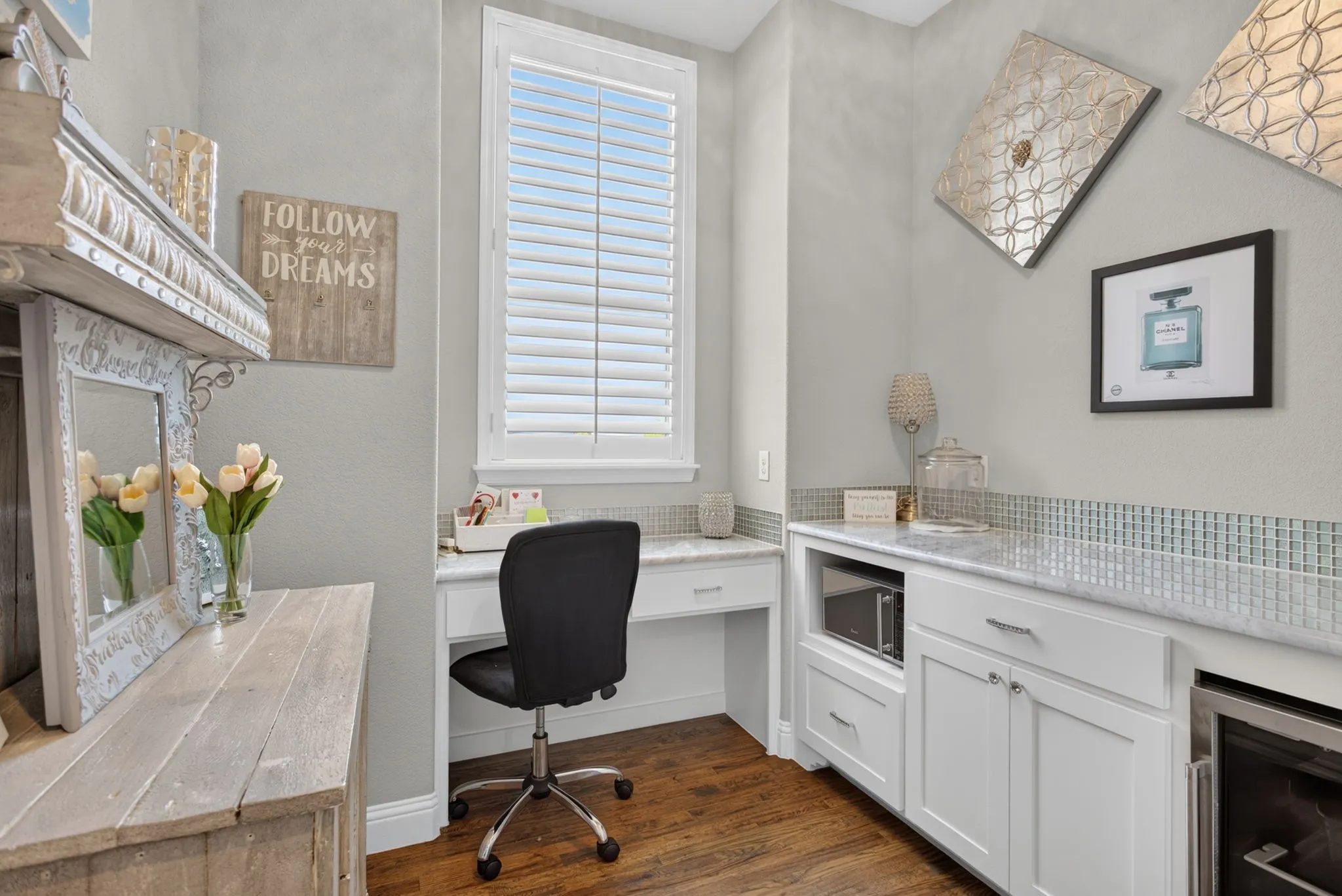 Integrated desk area featuring a window with plantation shutters, a light-toned countertop, and recessed white cabinetry