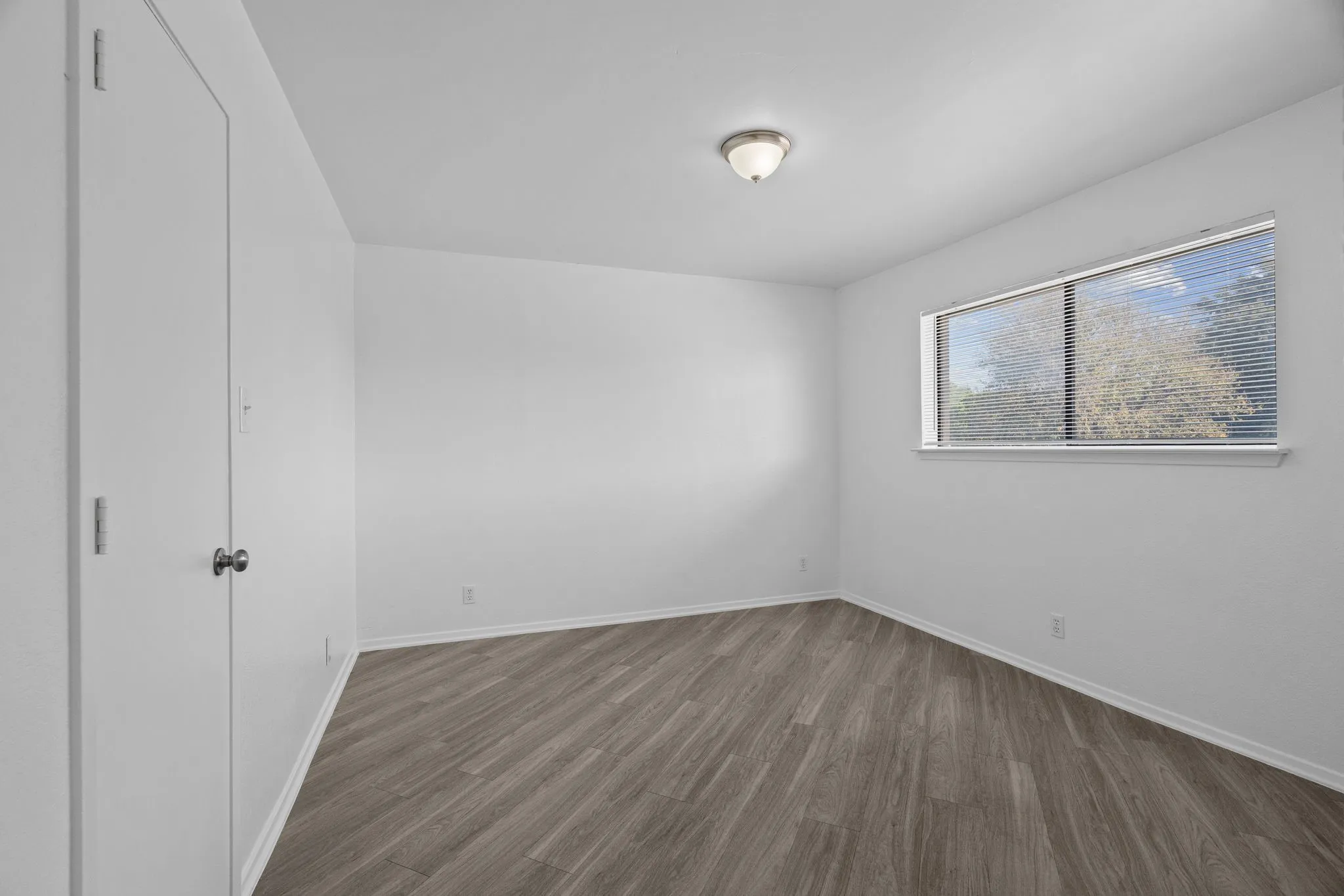 Room featuring wood-finish flooring, a double window with blinds, and a built-in closet with a bi-fold door and a standard door