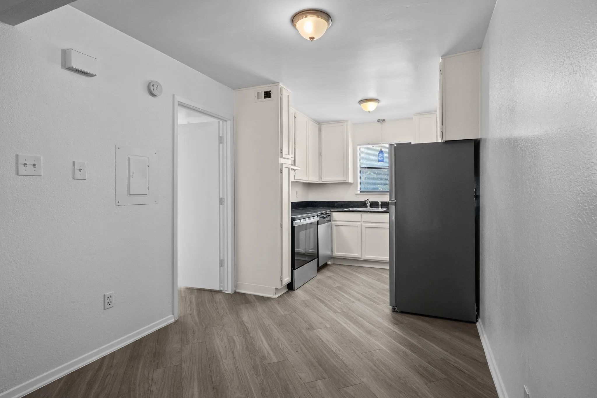 Kitchen with wood-finish flooring, white cabinetry, dark countertops, and stainless steel appliances