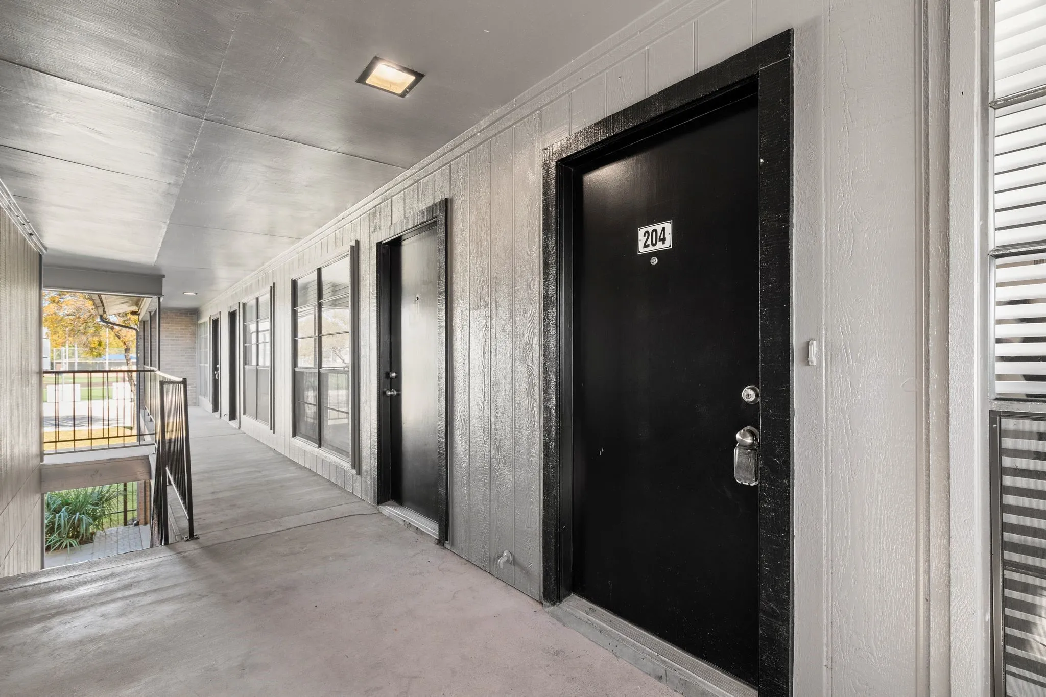 Exterior corridor featuring concrete flooring, a black metal railing, and a windowed wall