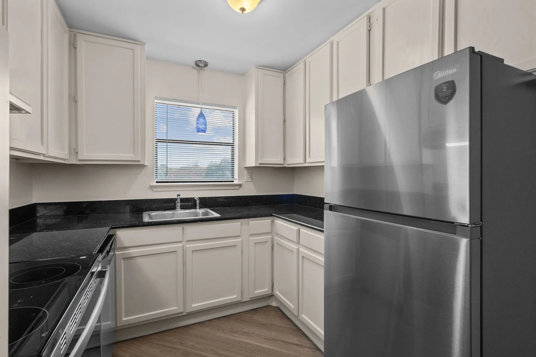 Efficient kitchen featuring light cabinetry, dark countertops, a stainless steel refrigerator, an electric range, and wood-finish flooring