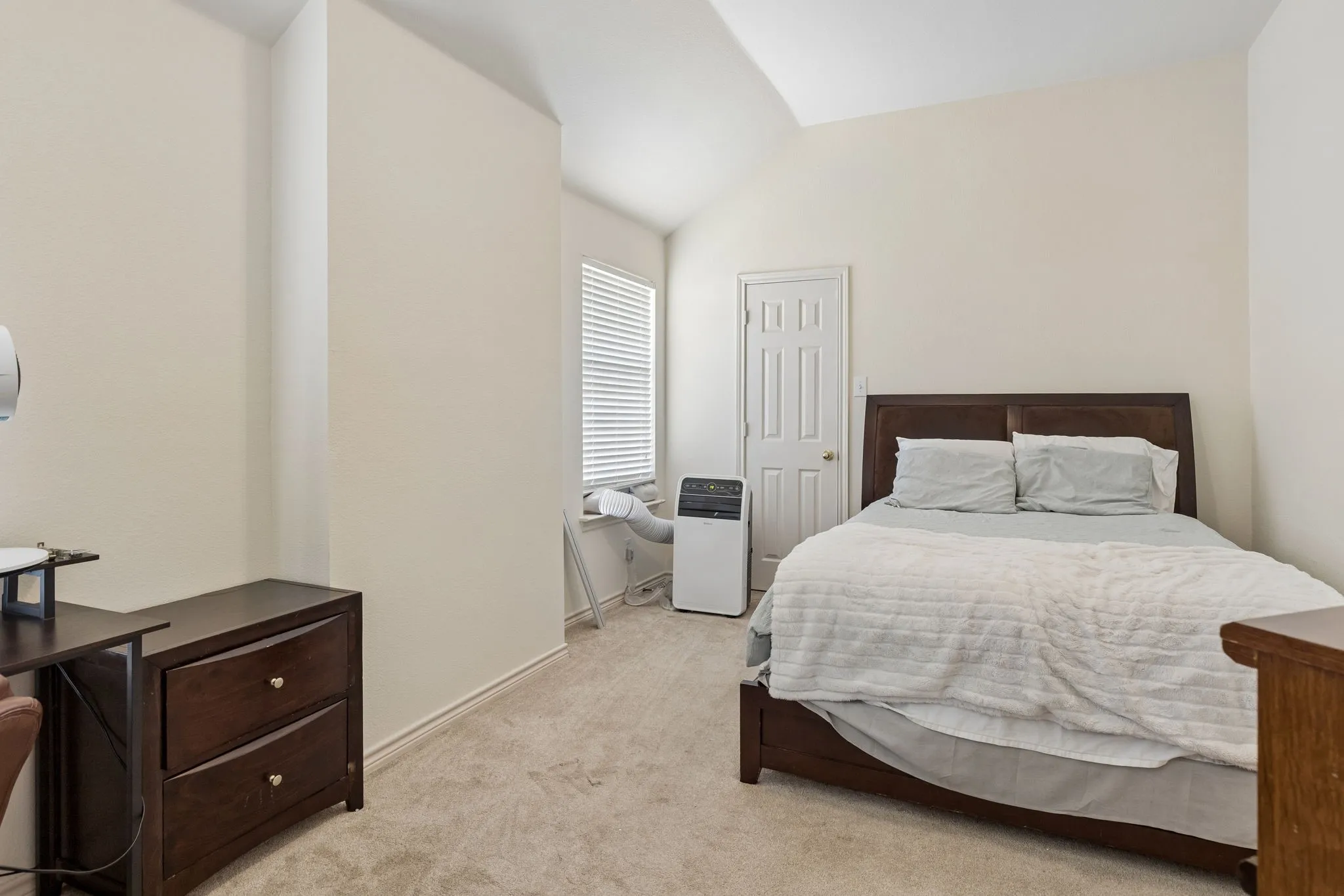 Vaulted ceiling bedroom featuring a panel door, window with blinds, and neutral carpeting