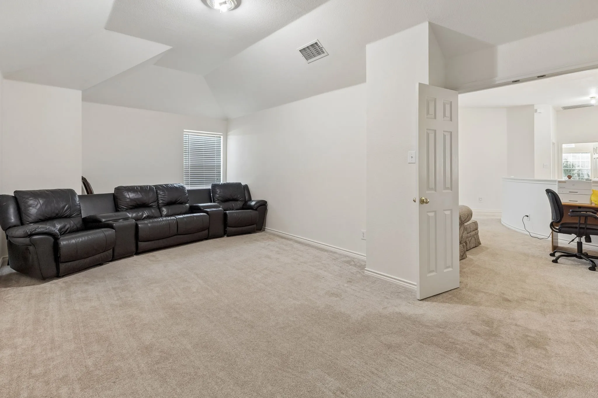 Spacious carpeted room featuring vaulted ceilings, a window with blinds, and white baseboards