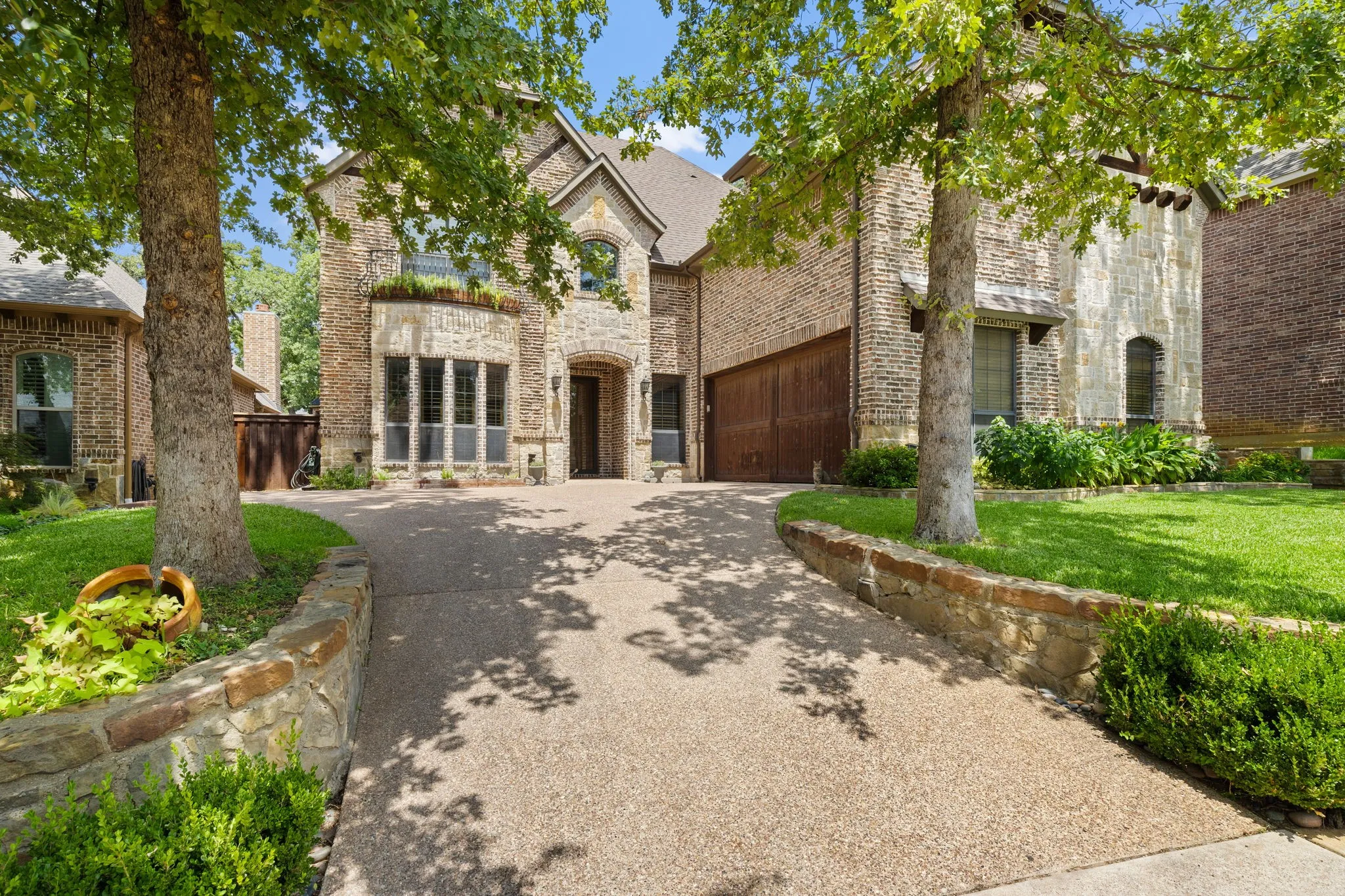 Brick and stone exterior with a peaked roofline, an arched entry, a multi-pane window bay, and an exposed aggregate driveway