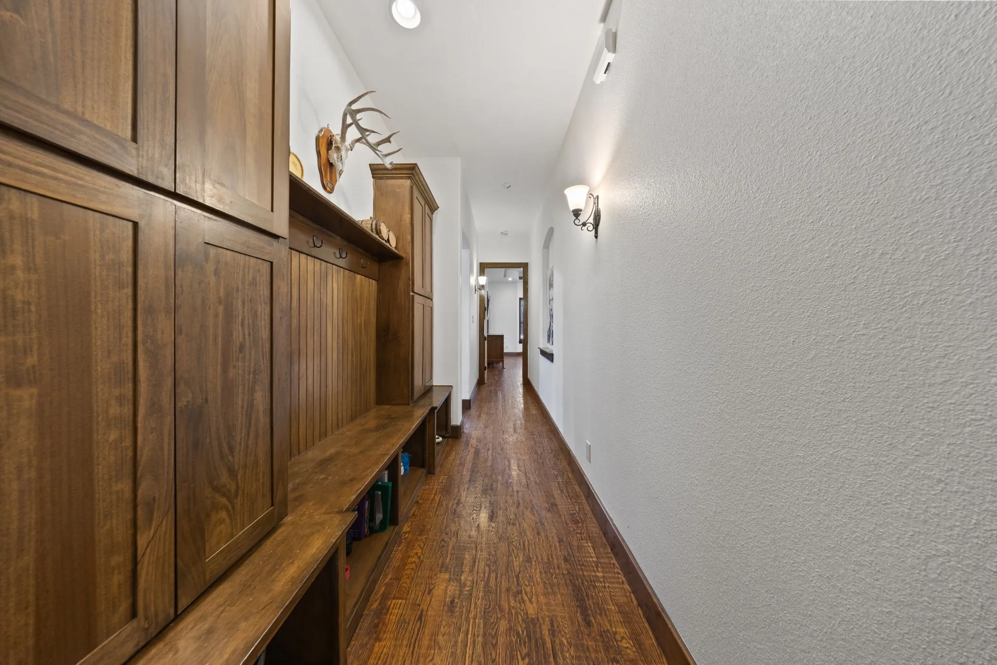 Mud room with wood-finish flooring extending through a hallway with built-in wood cabinetry and shelving