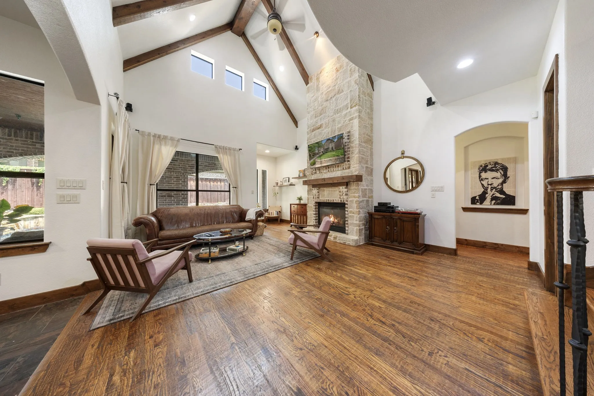 Vaulted ceiling featuring exposed beams, stone-clad fireplace with mantel, and wood-finish flooring
