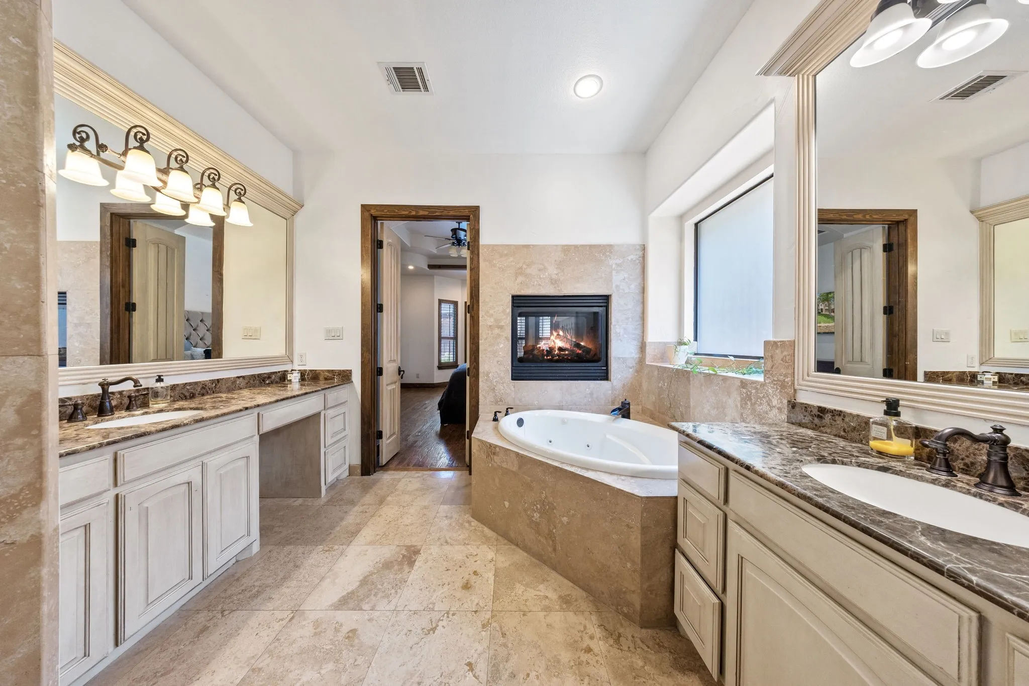 Dual vanity with undermount sinks, corner jetted tub, wall-mounted fireplace, and tile flooring