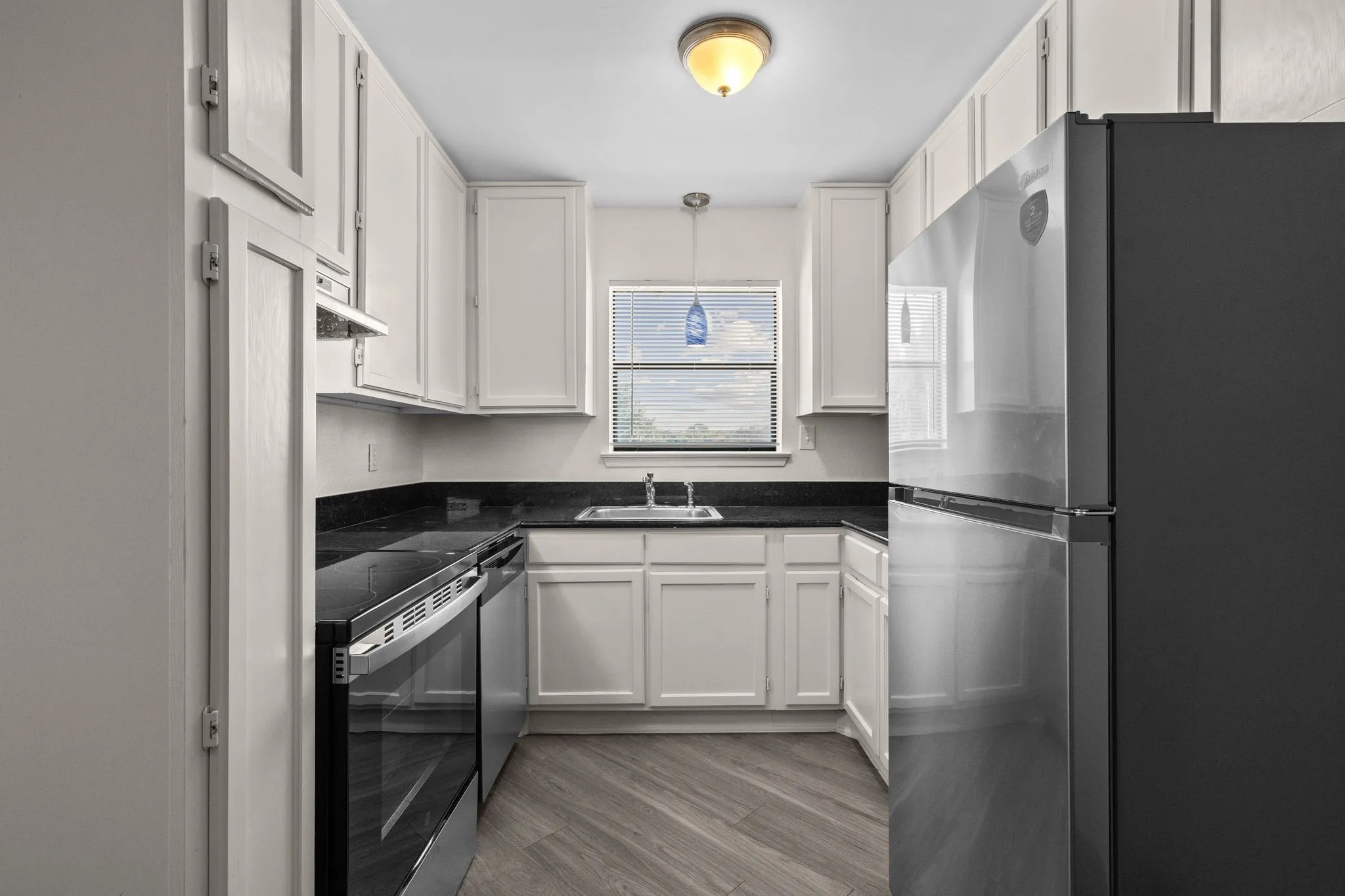 U-shaped kitchen featuring white cabinetry, dark countertops, a stainless steel refrigerator, and wood-finish flooring