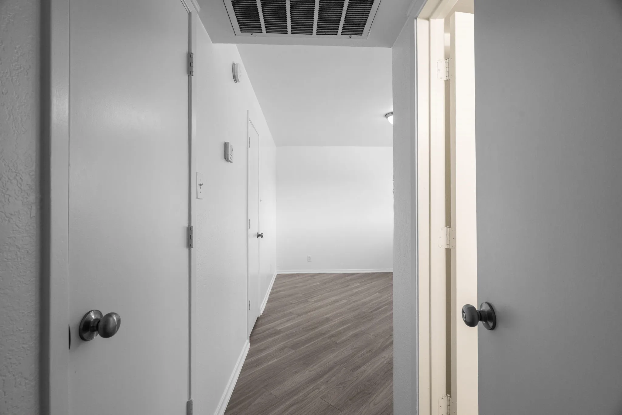Hallway featuring light gray wood-finish flooring, white walls, and multiple white doors with dark hardware