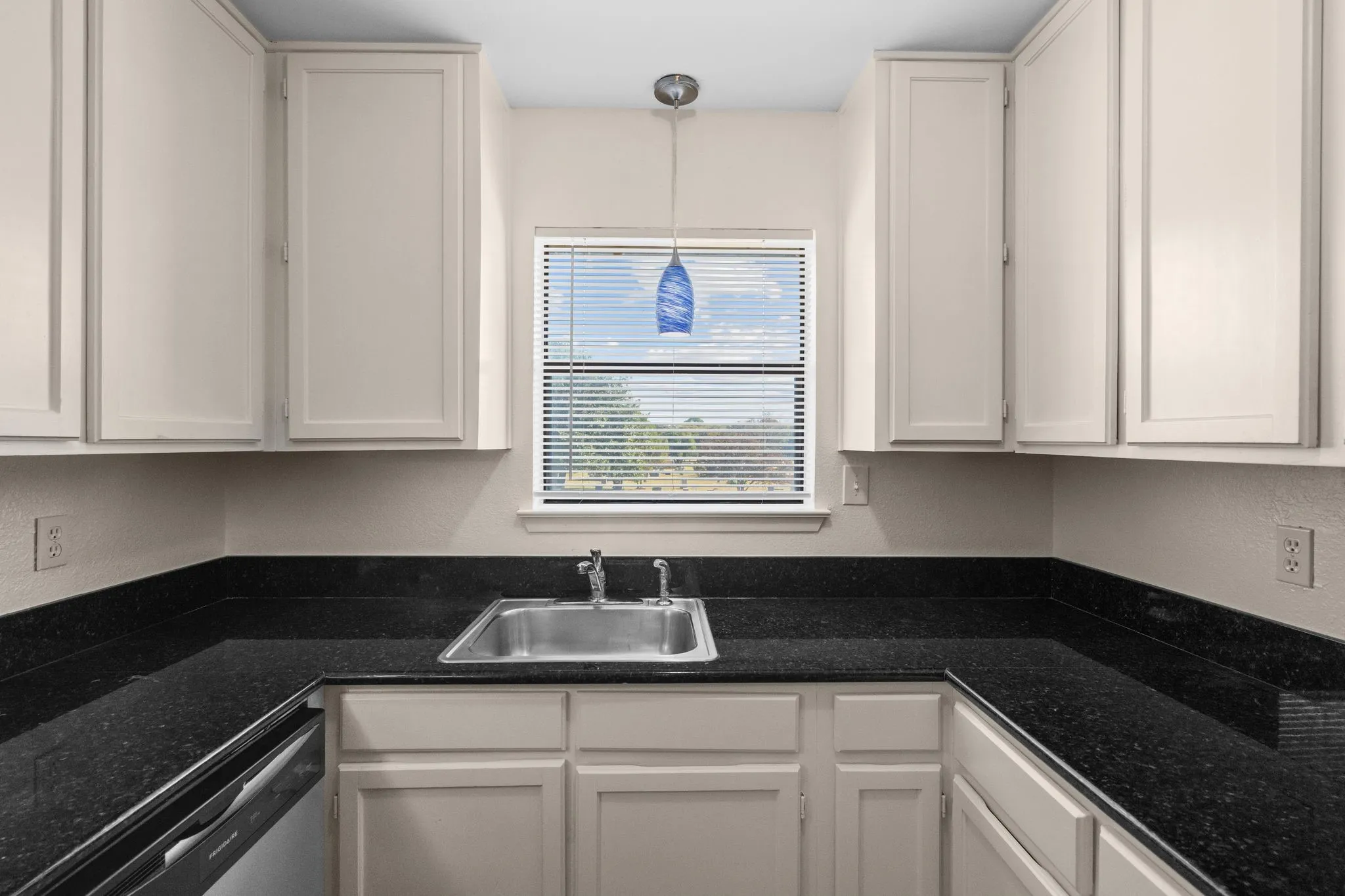 Kitchen featuring a stainless steel sink, dark speckled countertops, white cabinetry, a built-in dishwasher, and a window with blinds