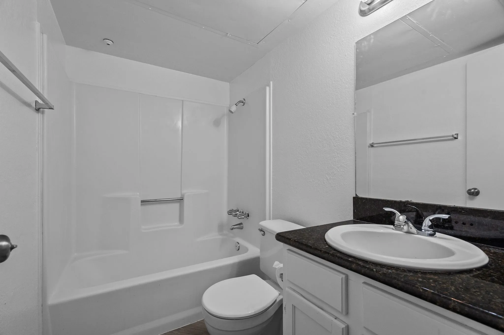 Bathroom featuring a white bathtub/shower combination, dark countertop vanity with an integrated sink, white vanity cabinetry, and wall-mounted mirror