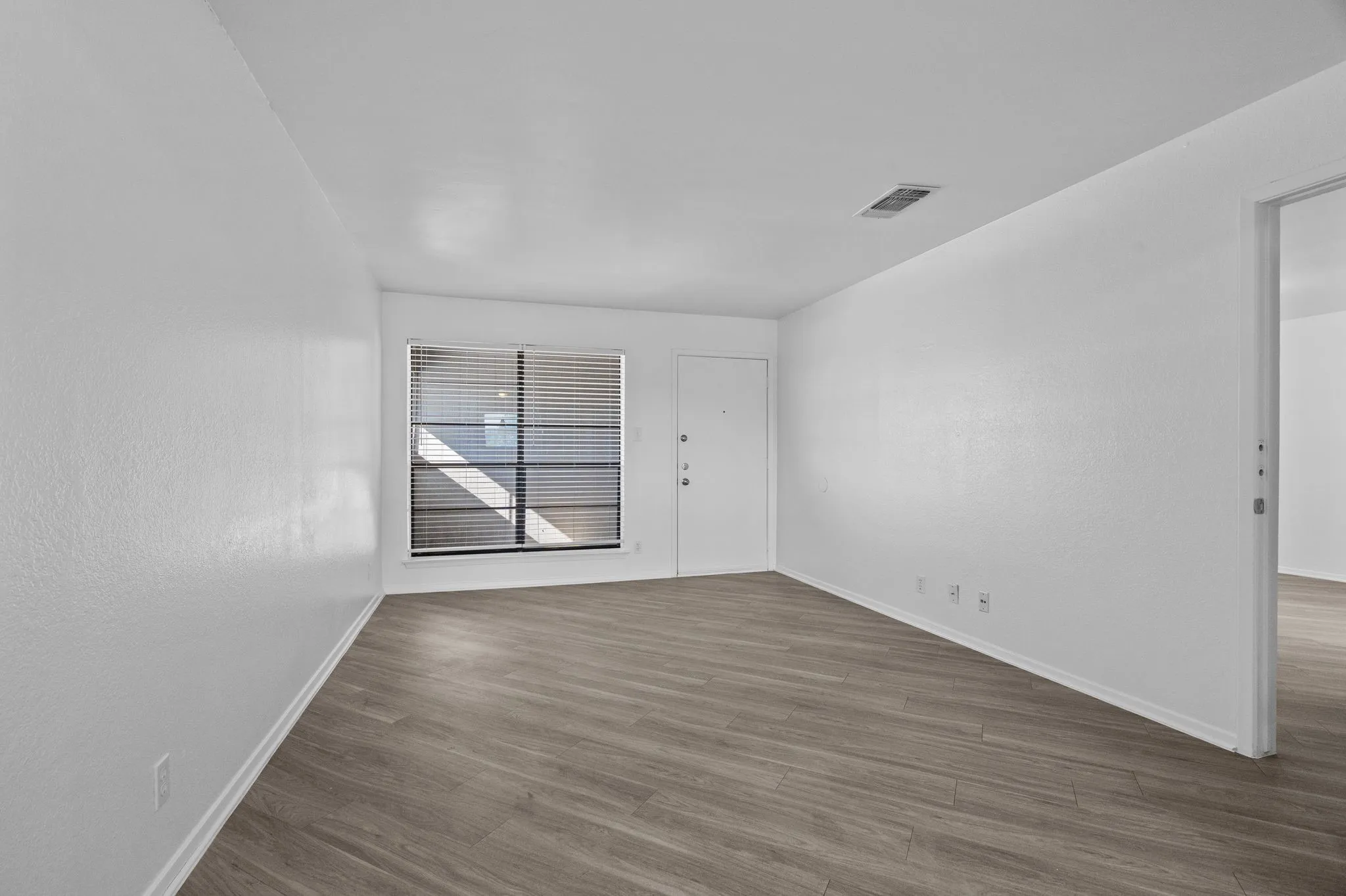 Spacious room featuring wood-finish flooring, white baseboards, and a large window with horizontal blinds