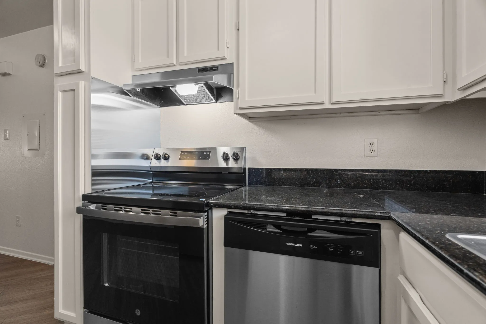 Kitchen featuring stainless steel appliances, dark speckled countertops, white cabinetry, and wood-finish flooring