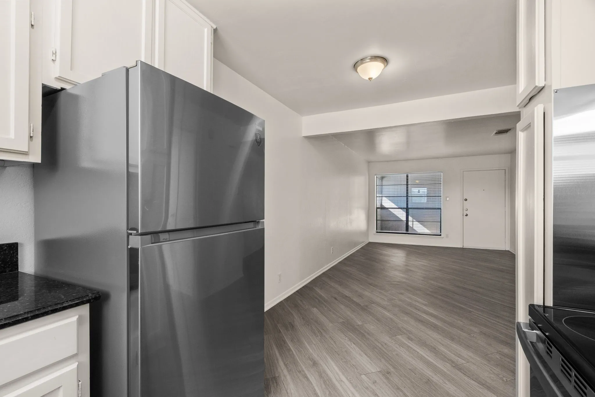 Kitchen area featuring a stainless steel refrigerator, white cabinetry, dark speckled countertop, and wood-finish flooring
