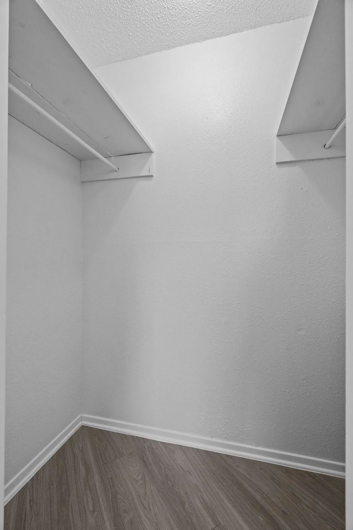 Interior closet featuring white walls, wood-finish flooring, white shelving, and hanging rods