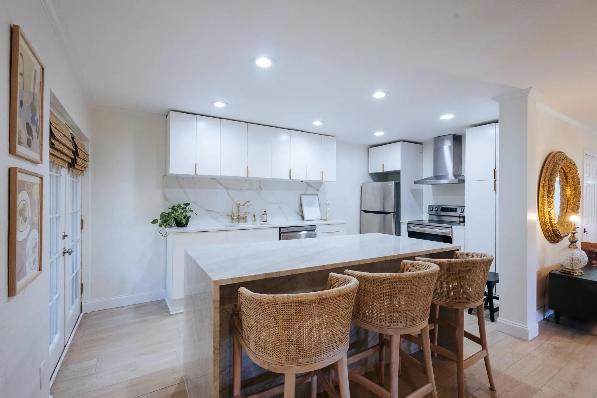 Contemporary kitchen with a waterfall island, white cabinetry, stainless steel appliances, a tile backsplash, and wood-finish flooring