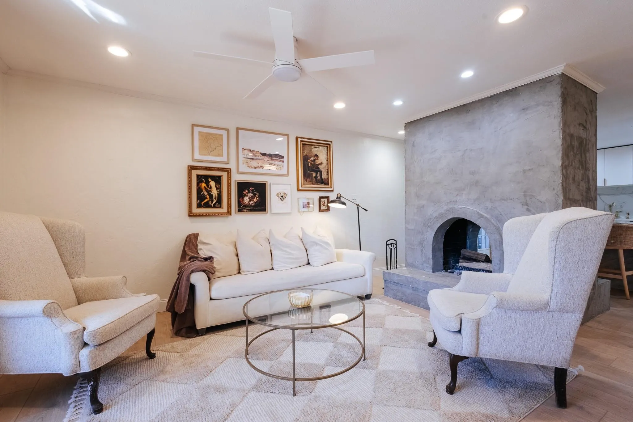 Living space featuring a prominent stucco-finished fireplace with an arched opening, recessed lighting, a ceiling fan, and wood-finish flooring