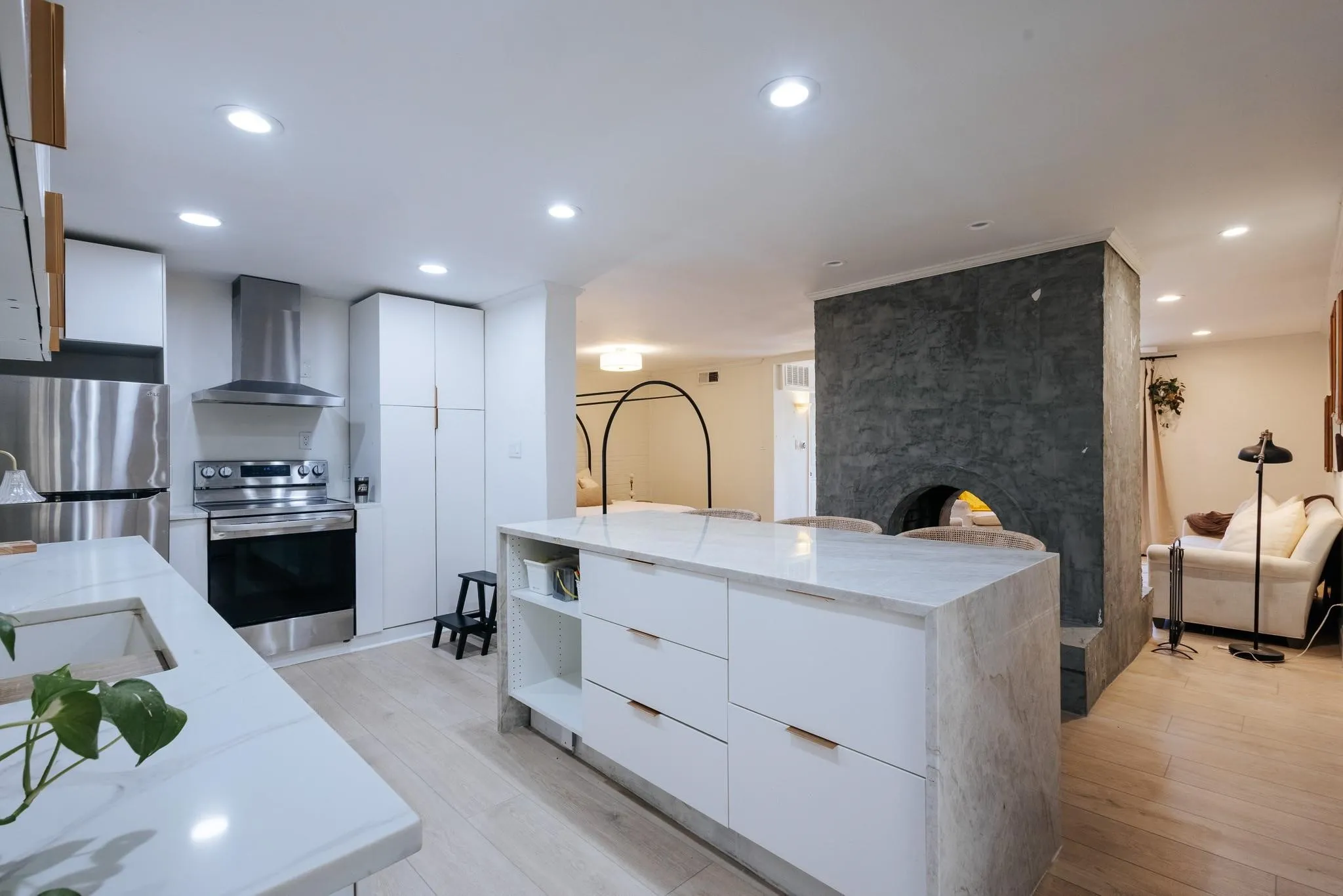 Modern kitchen featuring stainless steel appliances, white cabinetry, a waterfall island with integrated shelving, and recessed lighting