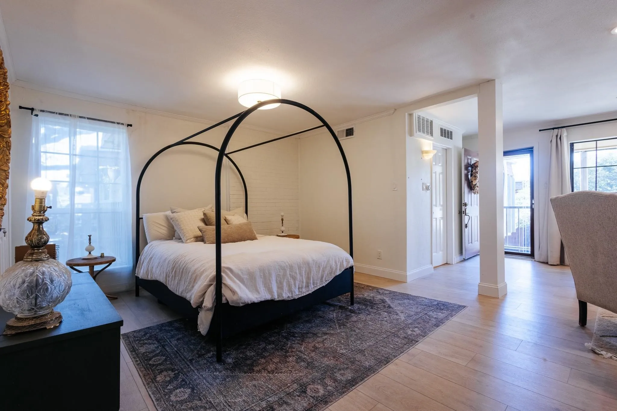 Spacious room featuring wood-finish flooring, white walls, and a large window with sheer curtains