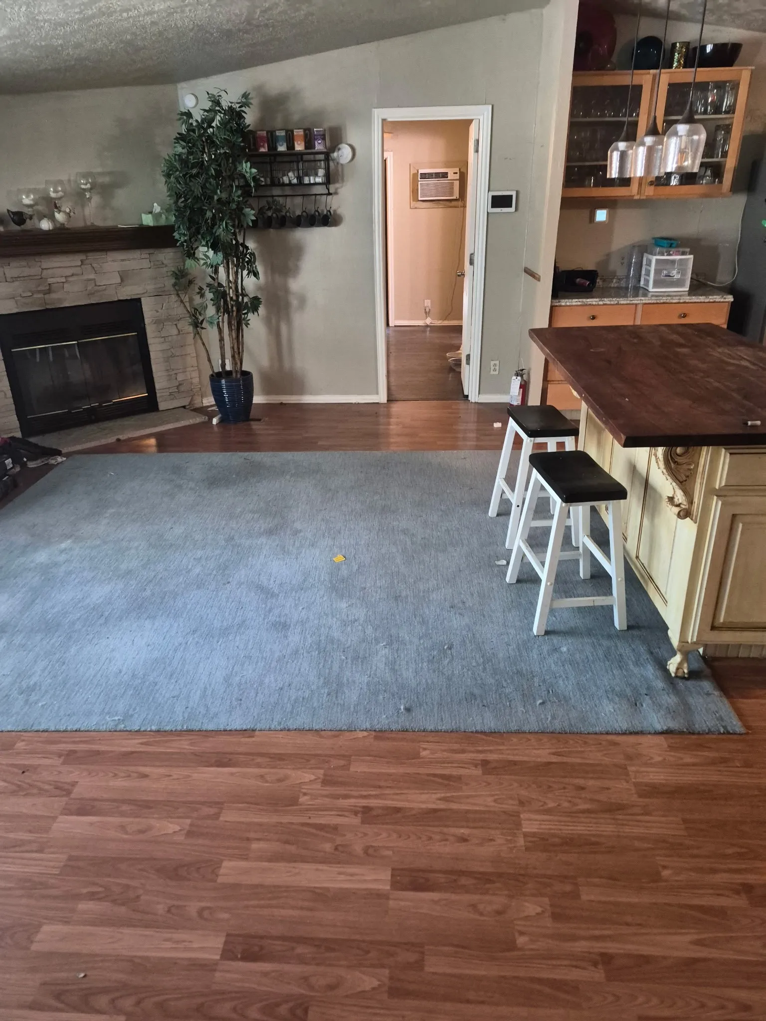 Wood-finish flooring leading to a stone-faced fireplace and a breakfast bar with a wood countertop