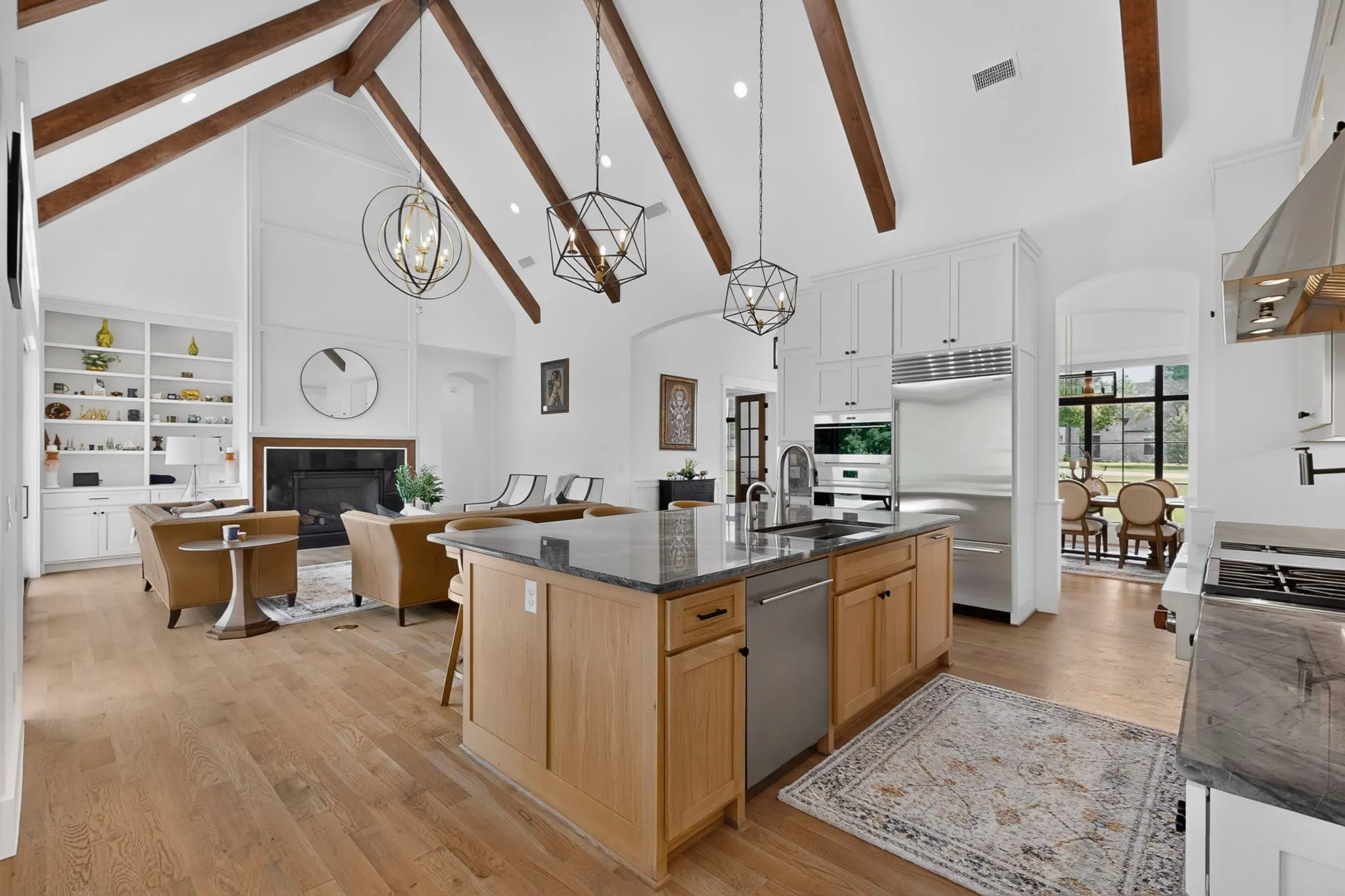 Open-concept kitchen and living area feature vaulted ceilings with exposed wood beams, woodflooring, a kitchen island with a dark countertop and undermount sink, and stainless steel appliances