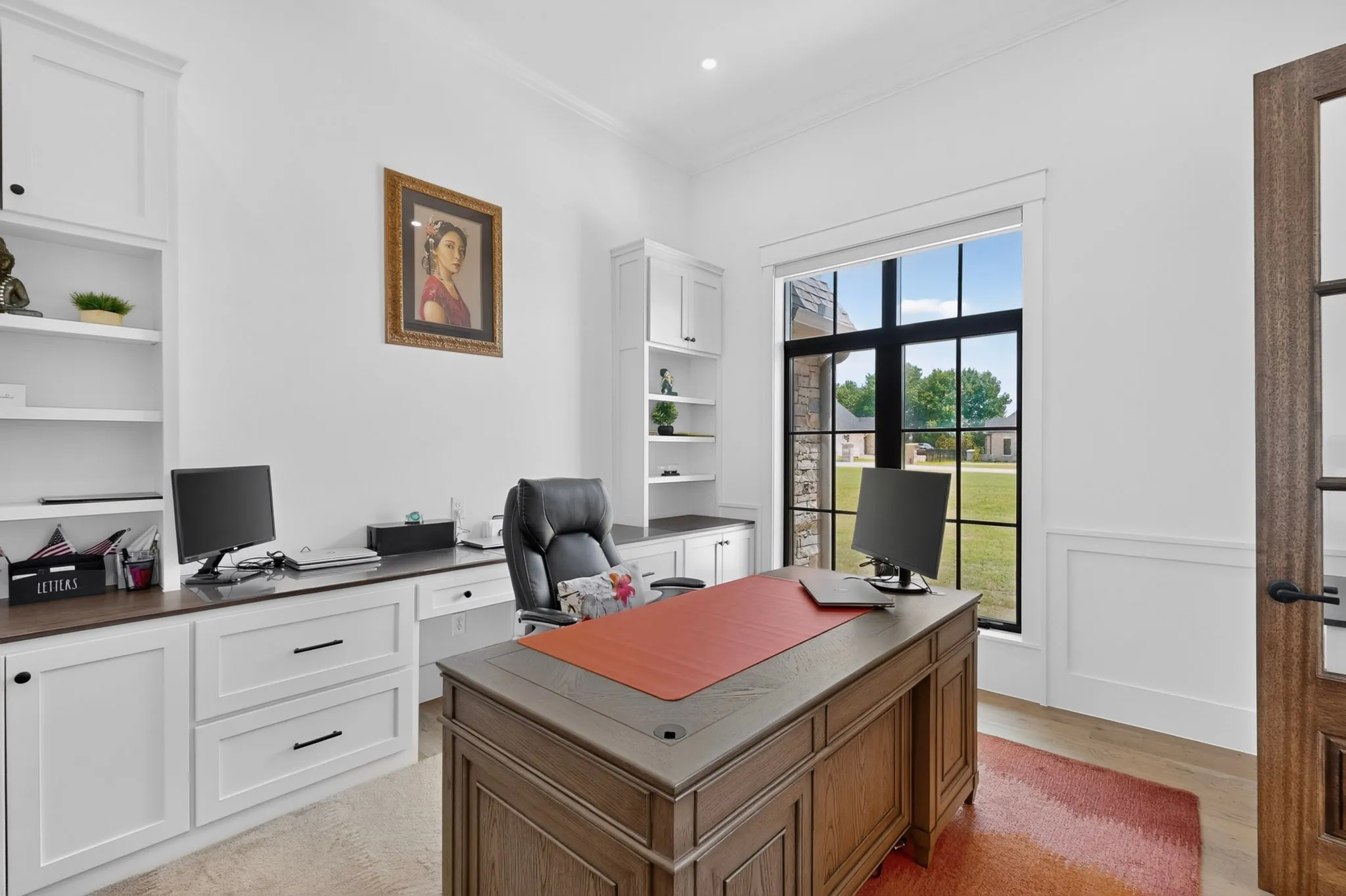A well designed, dedicated office space featuring extensive built-in white cabinetry, rich wood-finish countertops, and a large black-framed window just off the entryway