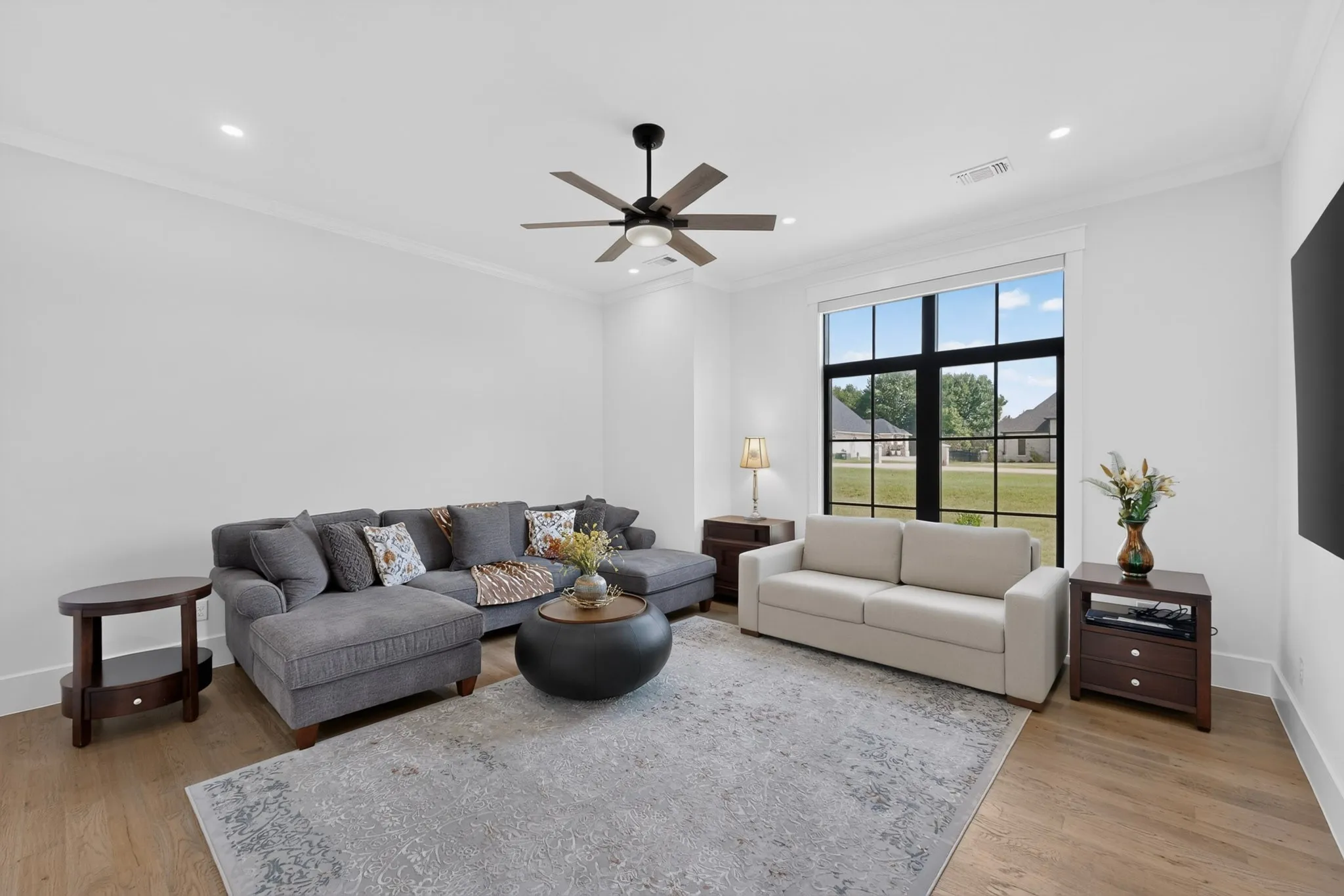 Spacious living area featuring light wood-finish flooring, recessed lighting, and a prominent black-framed window