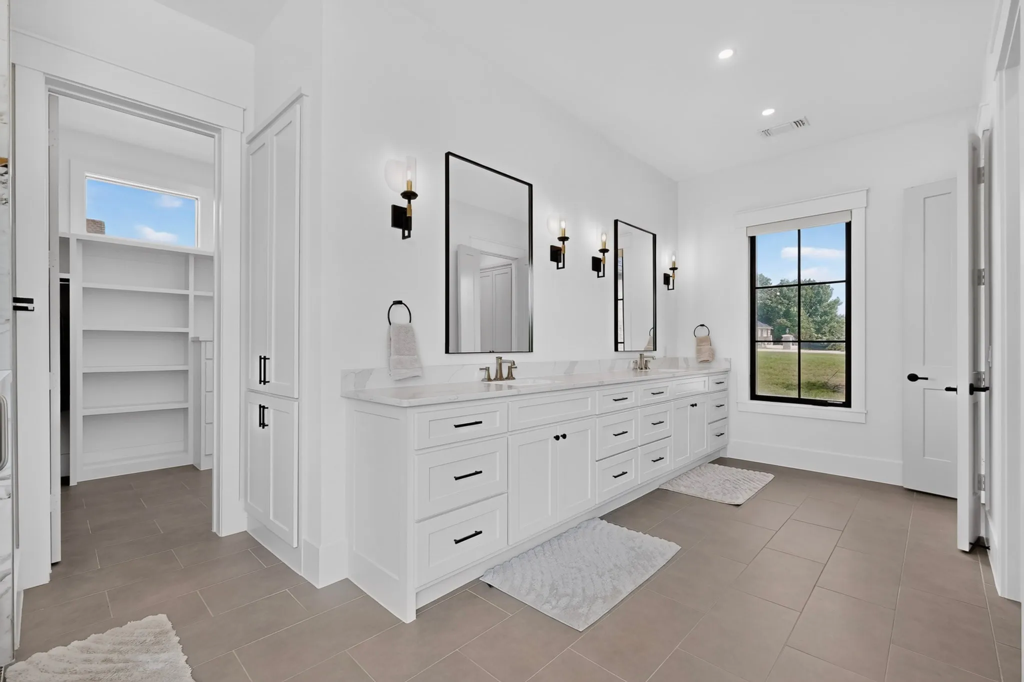 Spacious Primary Bathroom featuring a double vanity with white cabinetry, stone countertops, large format tile floor, and rectangular mirrors with black sconces