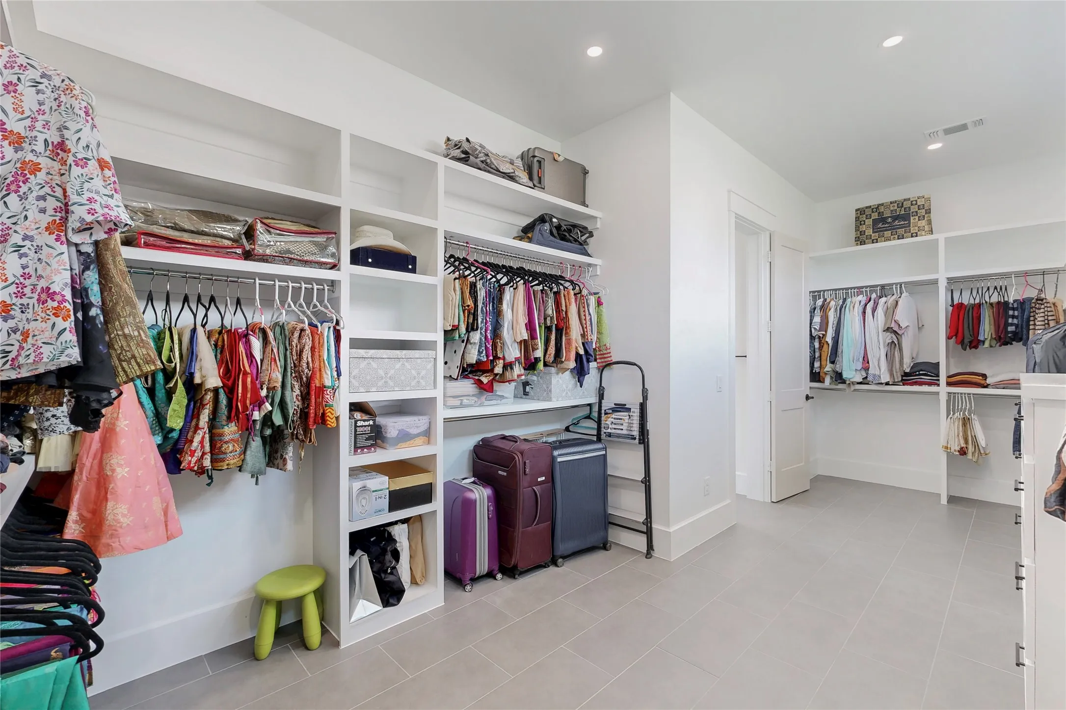 A second view of the spacious walk-in Primary closet featuring extensive built-in shelving, multiple hanging rods, recessed lighting, and light-toned tile flooring