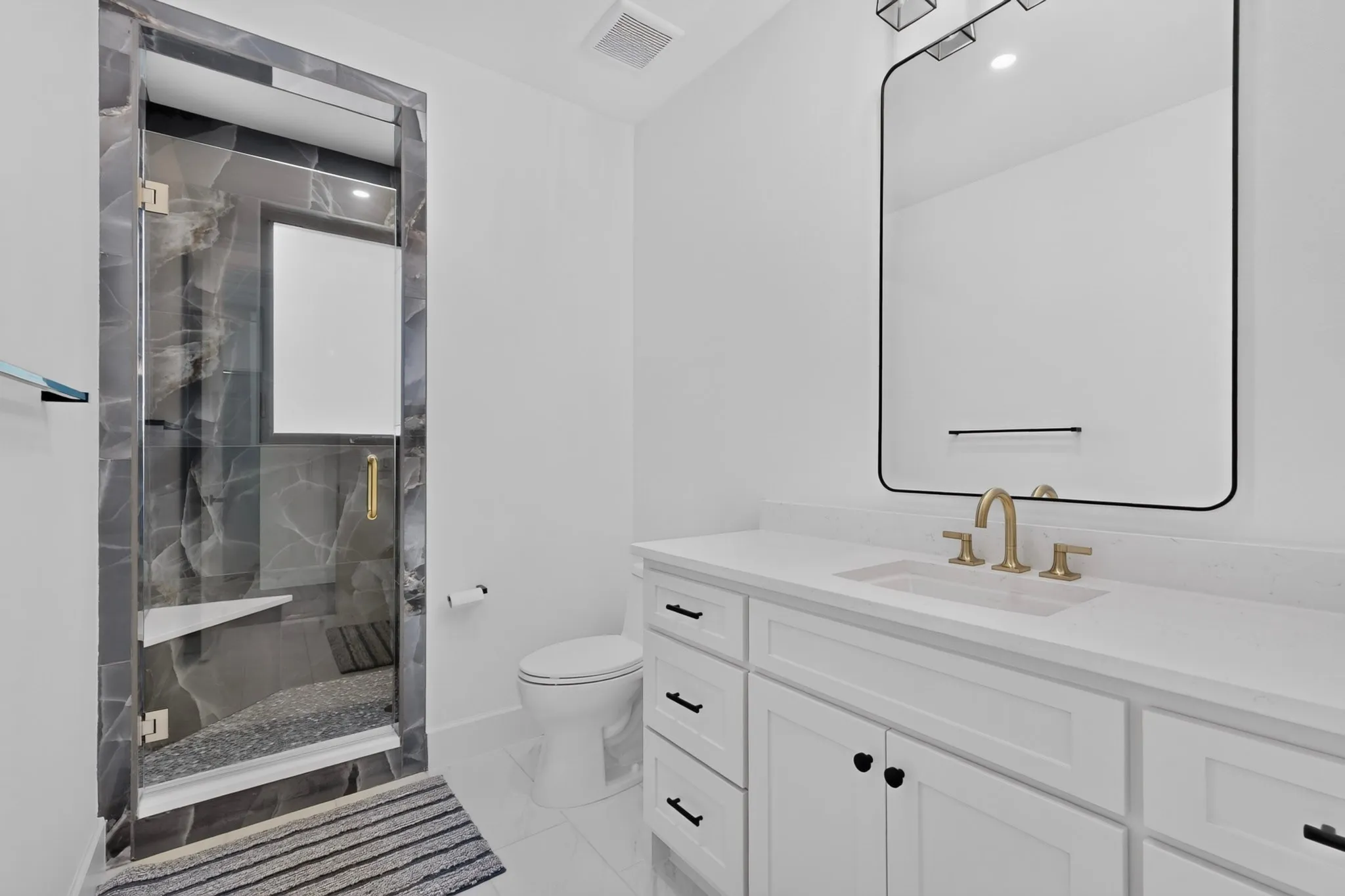 Upstairs modern bathroom featuring a frameless glass shower enclosure with dark marbled tile, an integrated shower bench, and pebble-style flooring
