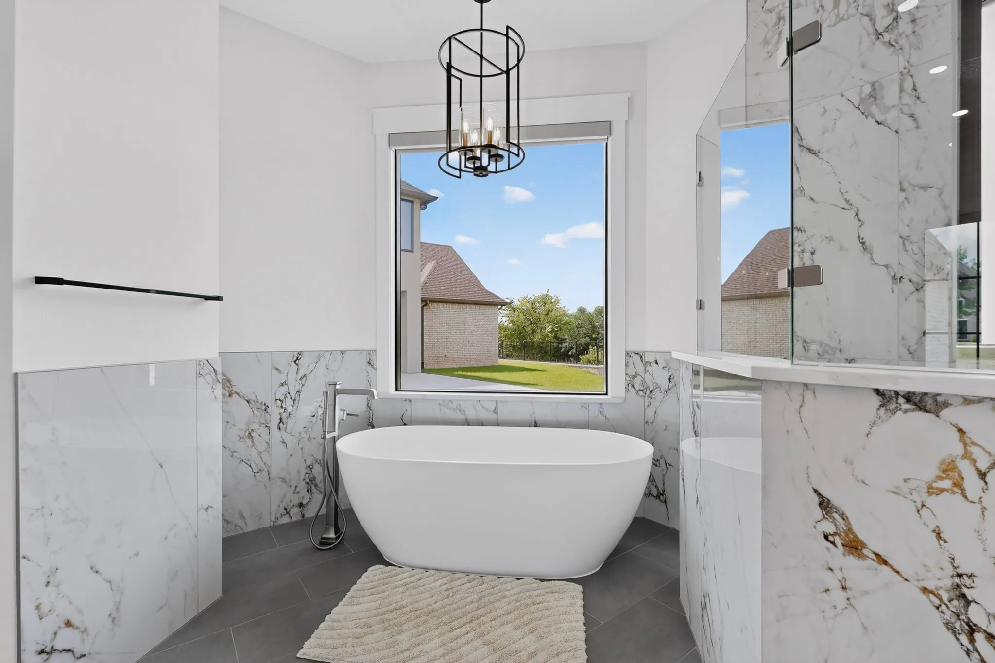 Primary Bathroom wet area features a freestanding soaking tub, large picture window, and extensive large format marble-look tile in the shower