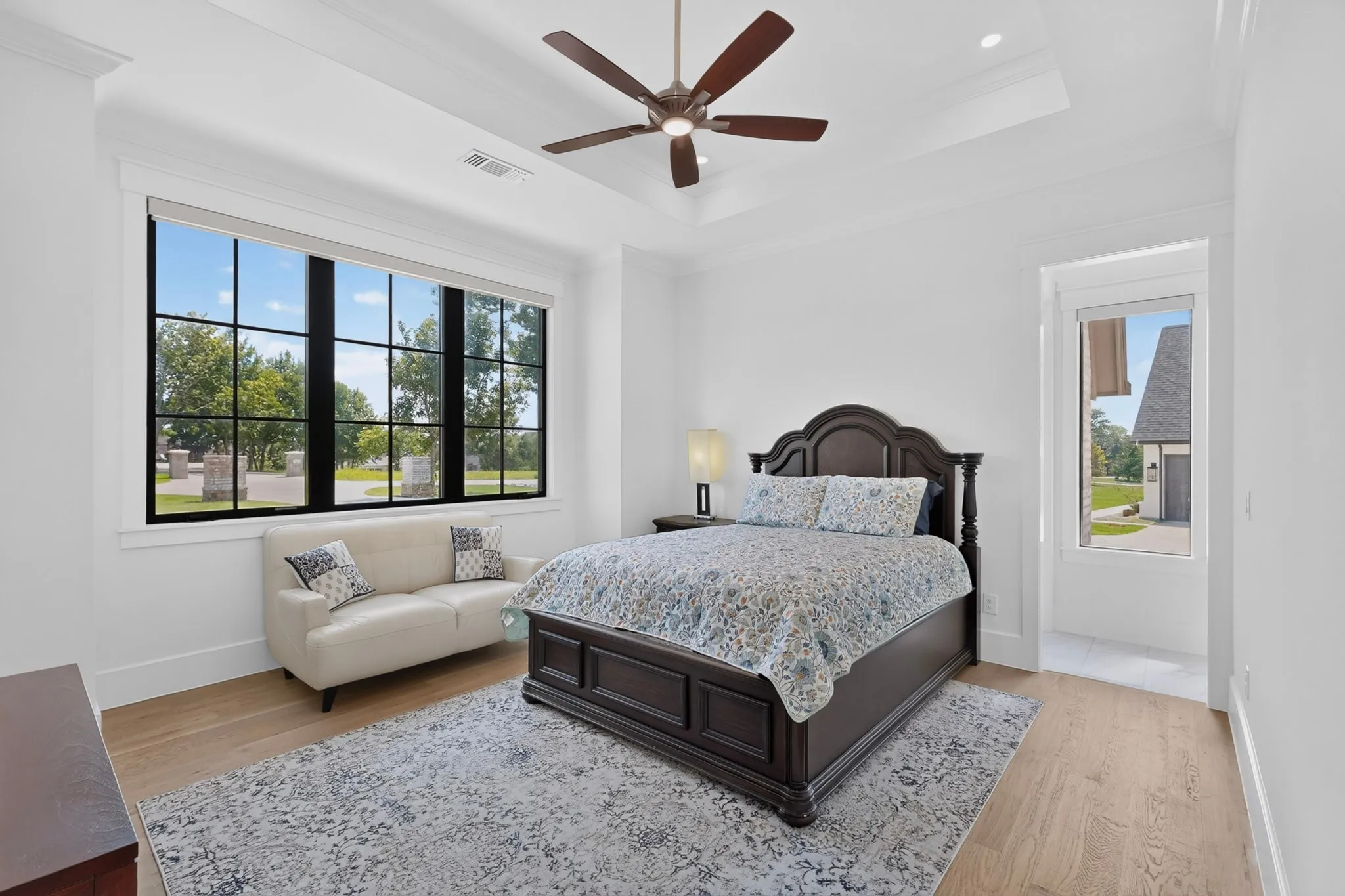 Spacious 2nd bedroom featuring a large gridded window, ceiling fan, tray ceiling, wood-finish flooring, and recessed lighting