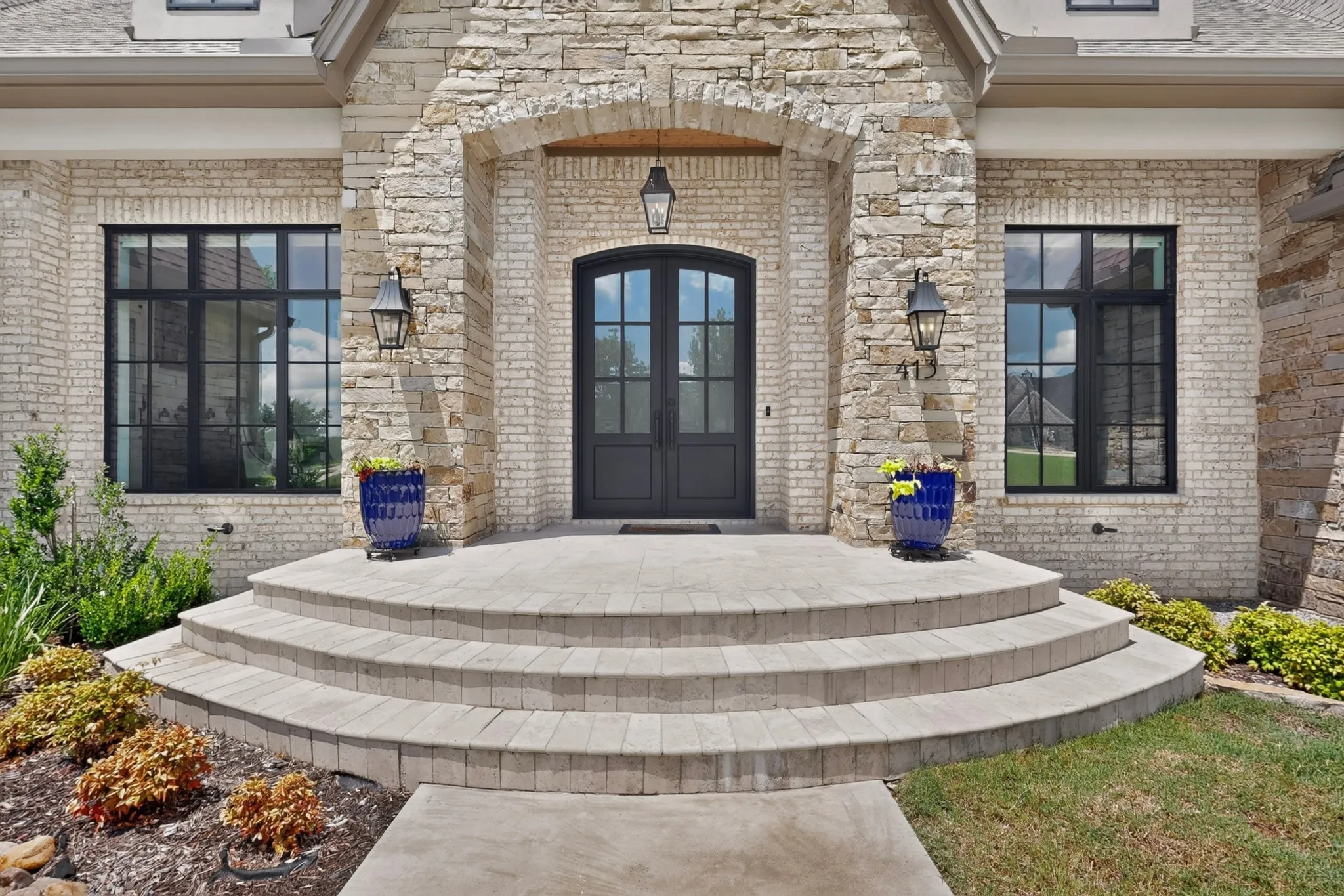 Arched double entry doors flanked by black-framed grid windows greet guests at front door.