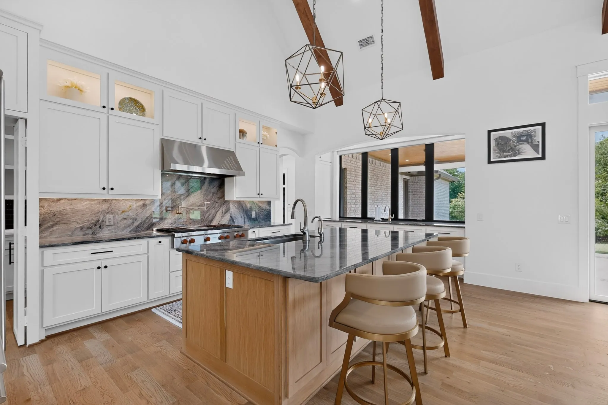 Kitchen featuring a large island with stone countertop, stainless steel appliances, custom cabinetry with under-cabinet lighting, upper cabinet lighting, natural wood-finish flooring, and vaulted ceiling with exposed stained  beams