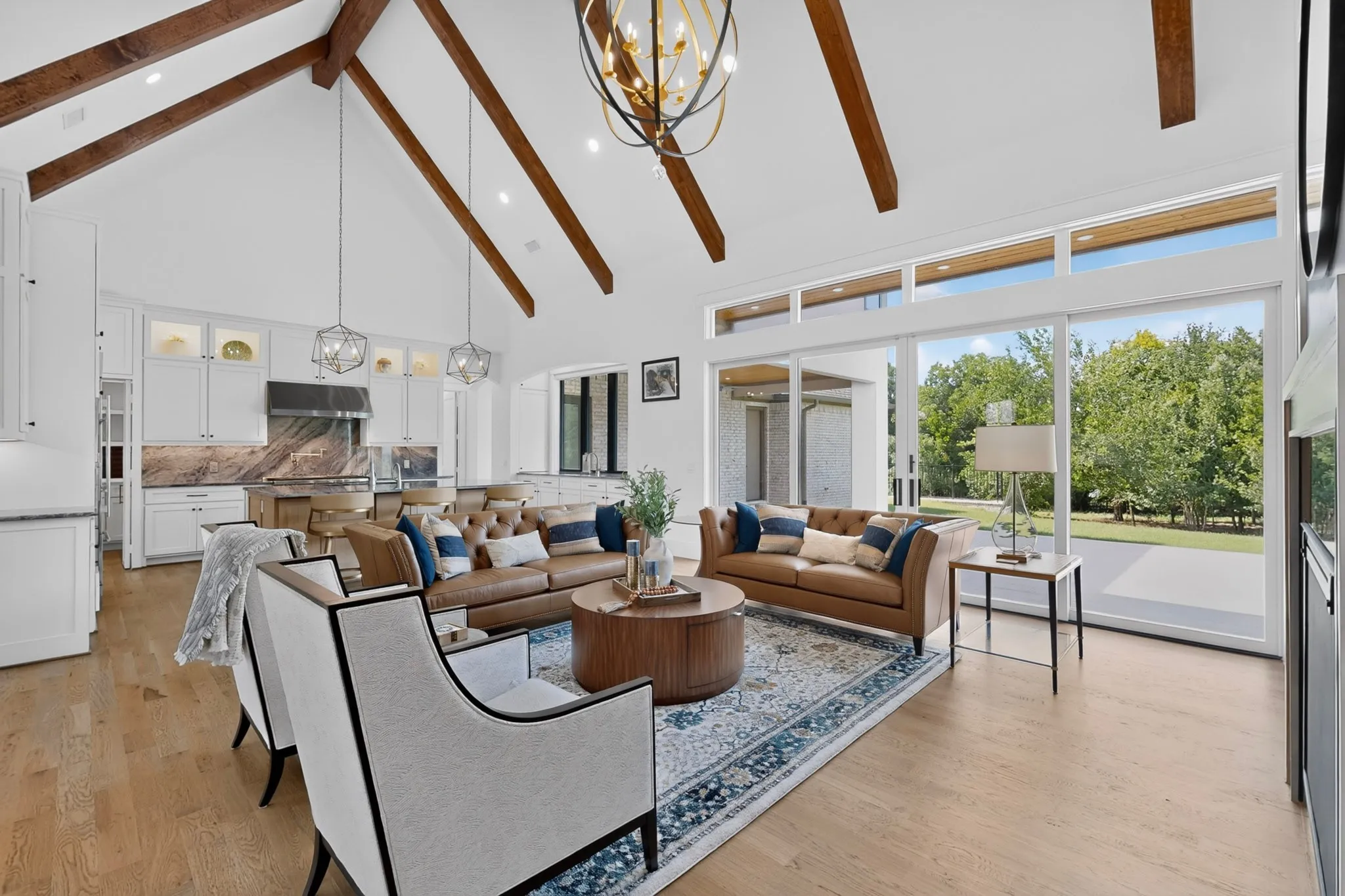 Expansive great room featuring vaulted ceilings with exposed wood beams, a contemporary chandelier, and wood-finish flooring
