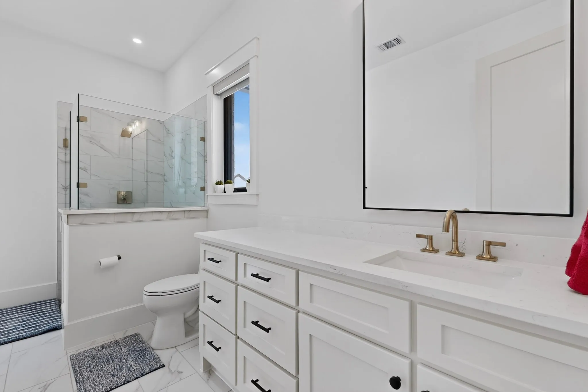 Bathroom featuring a spacious vanity with an integrated sink, brushed gold fixtures, and a large framed mirror